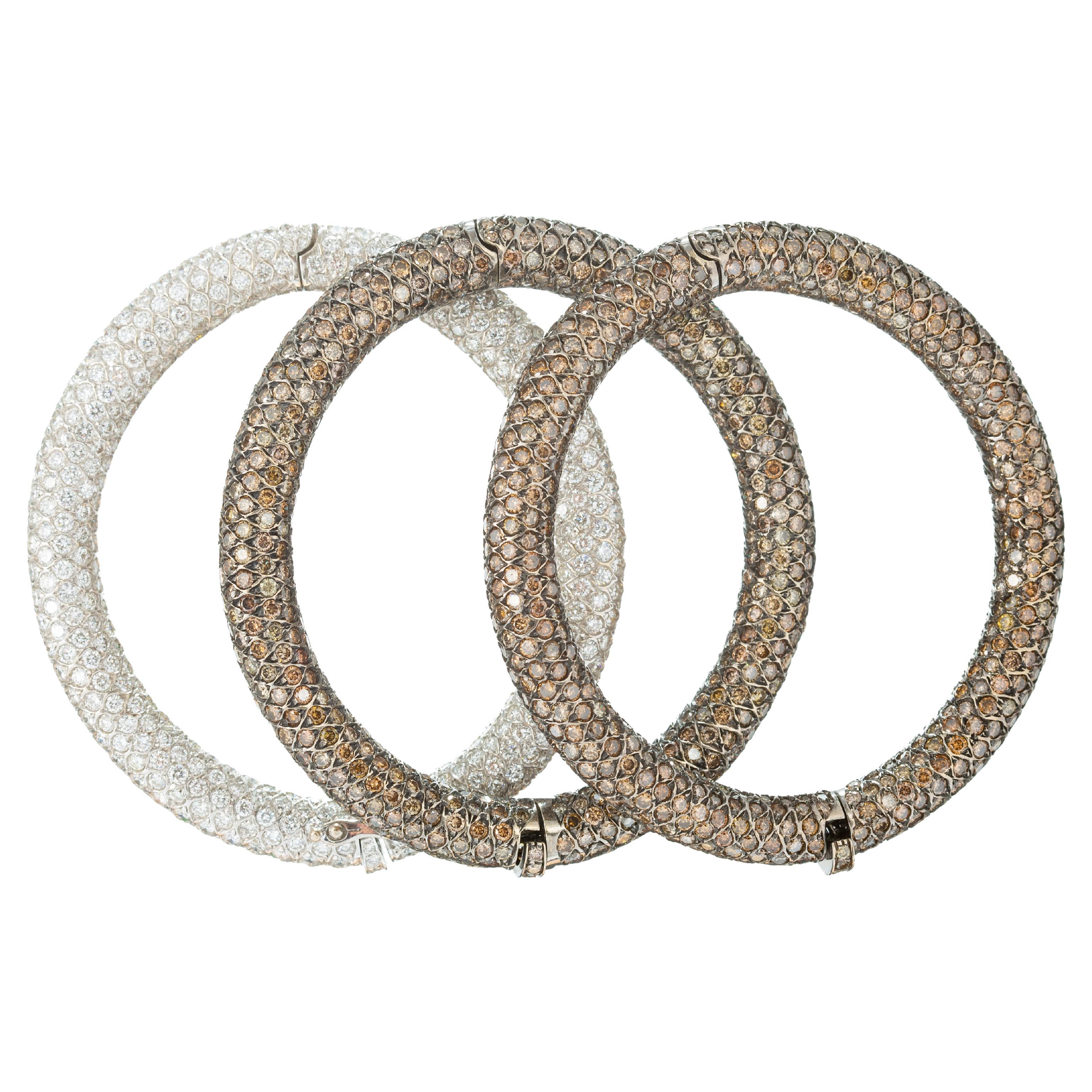 Three diamond bangle bracelets in 18k white gold, pave' set with champagne and white diamonds throughout.  One bracelet is set with four hundred thirty-seven round brilliant-cut 'white' diamonds; and two matching design bracelets in a blackened 18k