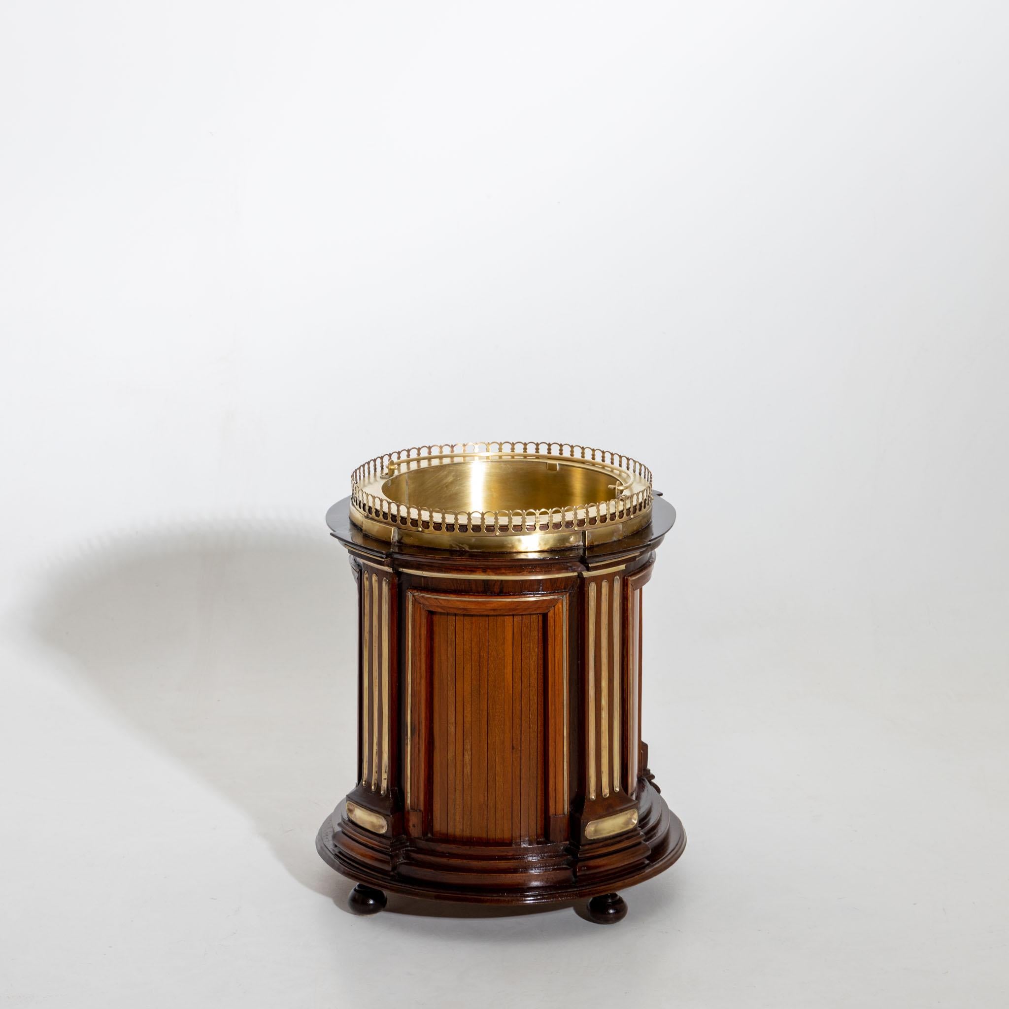 Champagne cooler with brass gallery rail and wooden case with fluted pilasters and round profiled base. The cylindrical insert is in polished brass.