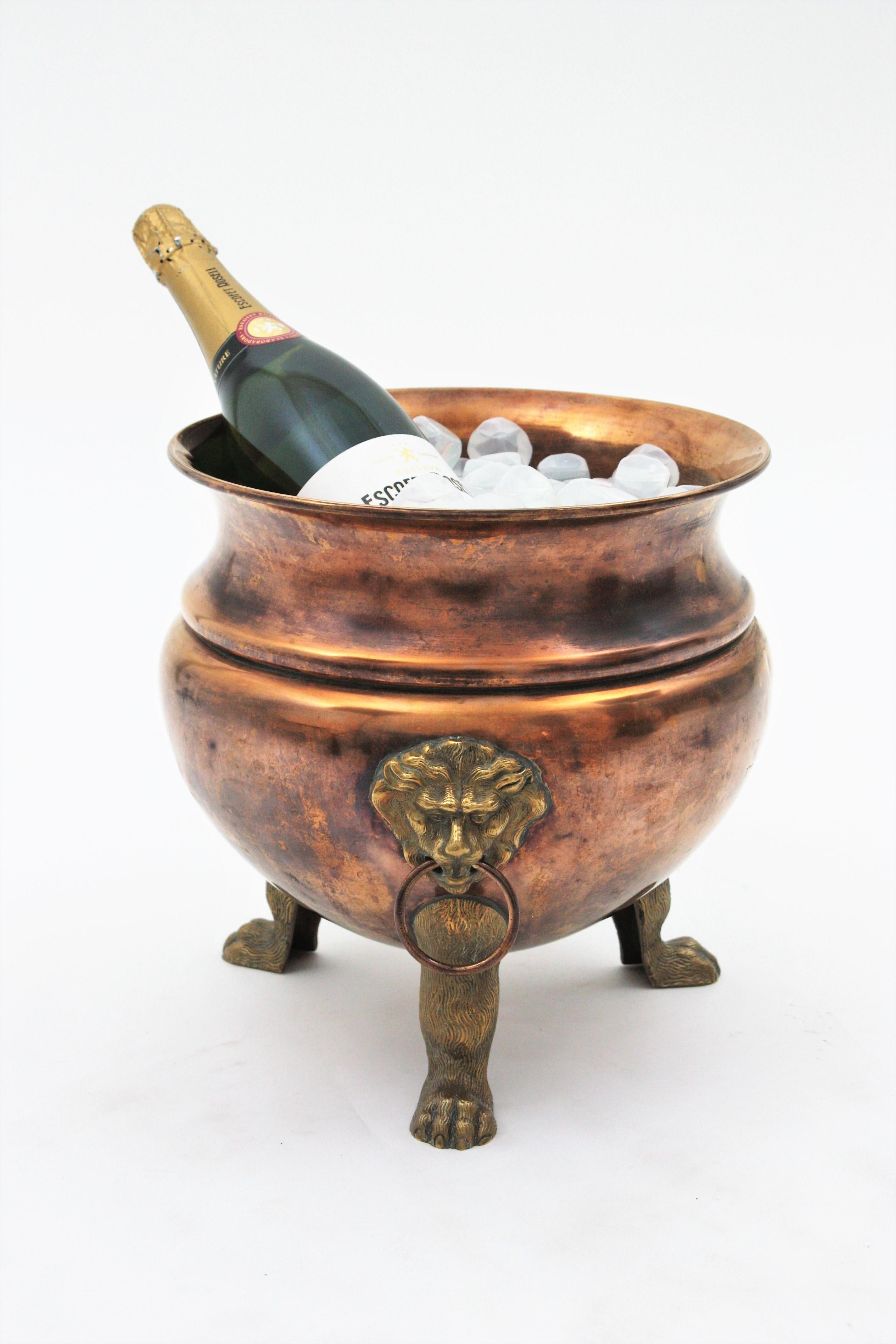 Copper and brass wine cooler or jardinière, Regency Style, England, 1930s
This round copper pot is finely executed in hand-hammered copper and it is supported by tripod paw feet. At both sides it has lion heads holding copper rings in their mouths