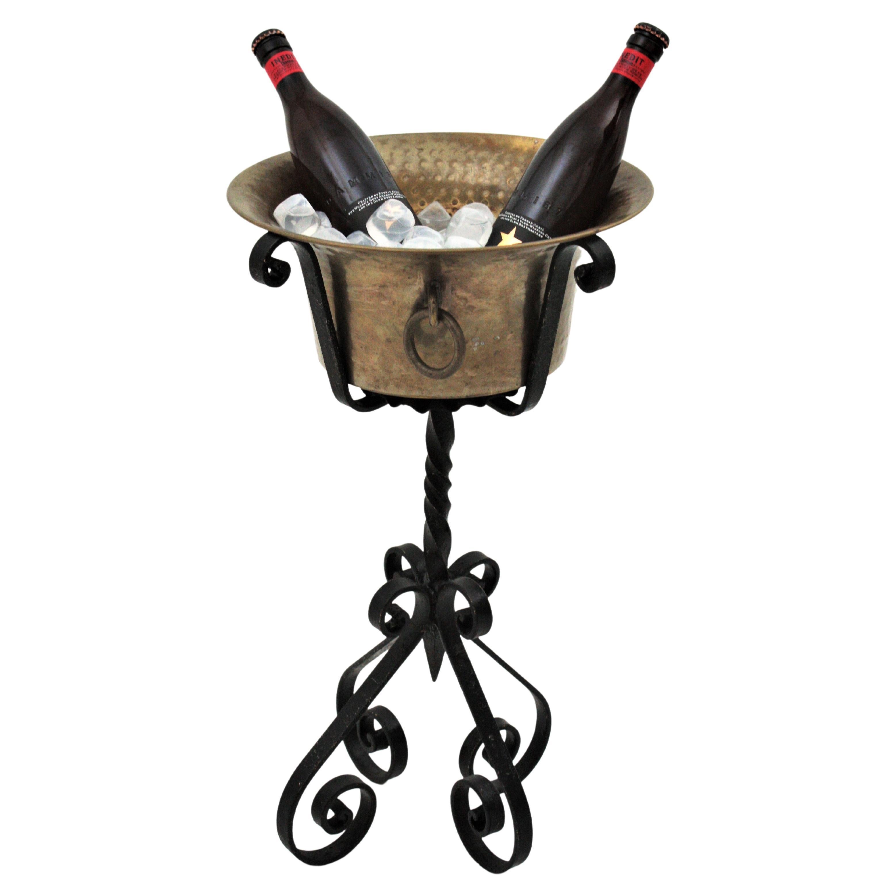 Spanish Colonial Wrought iron stand with with hand-hammered brass ice bucket, Spain, 1930s-1940s.
This pedestal champagne serving stand is all made by hand. The handwrought iron stand has a four footed base with scrolled endings, twisting details on