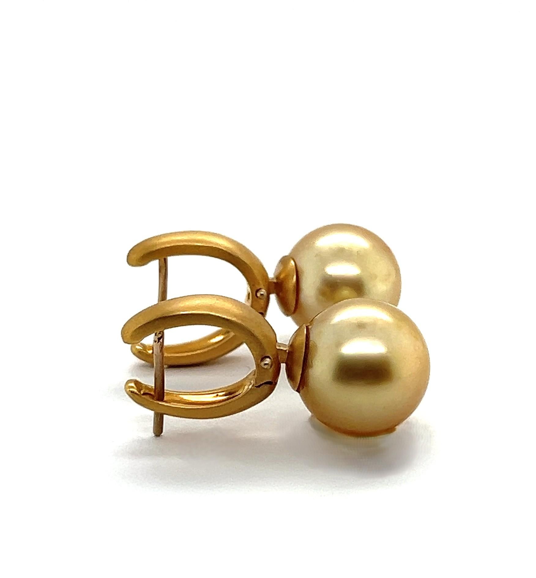 These sophisticated drop earrings feature luminous champagne-colored pearls delicately suspended from finely crafted gold settings. Their timeless silhouette combines classic elegance with a hint of modern luxury. The pearls, known for their soft