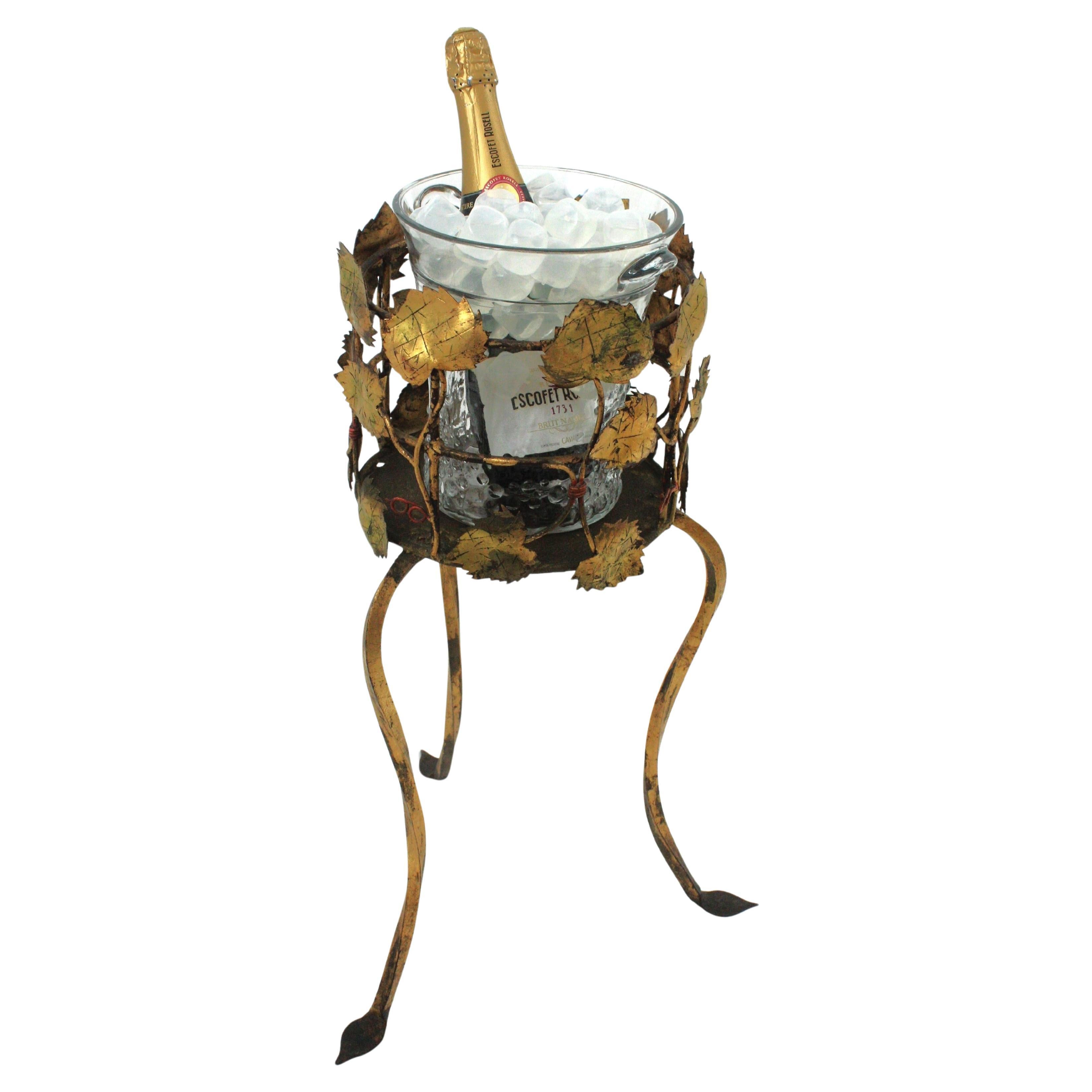 One of a kind foliage gilt iron tripod stand with pressed glass ice bucket, Spain, 1940s
This iron ice bucket serving stand is all made by hand. The handwrought iron stand has a leafed richly adorned top showing gilt iron vine leaves thorough. It
