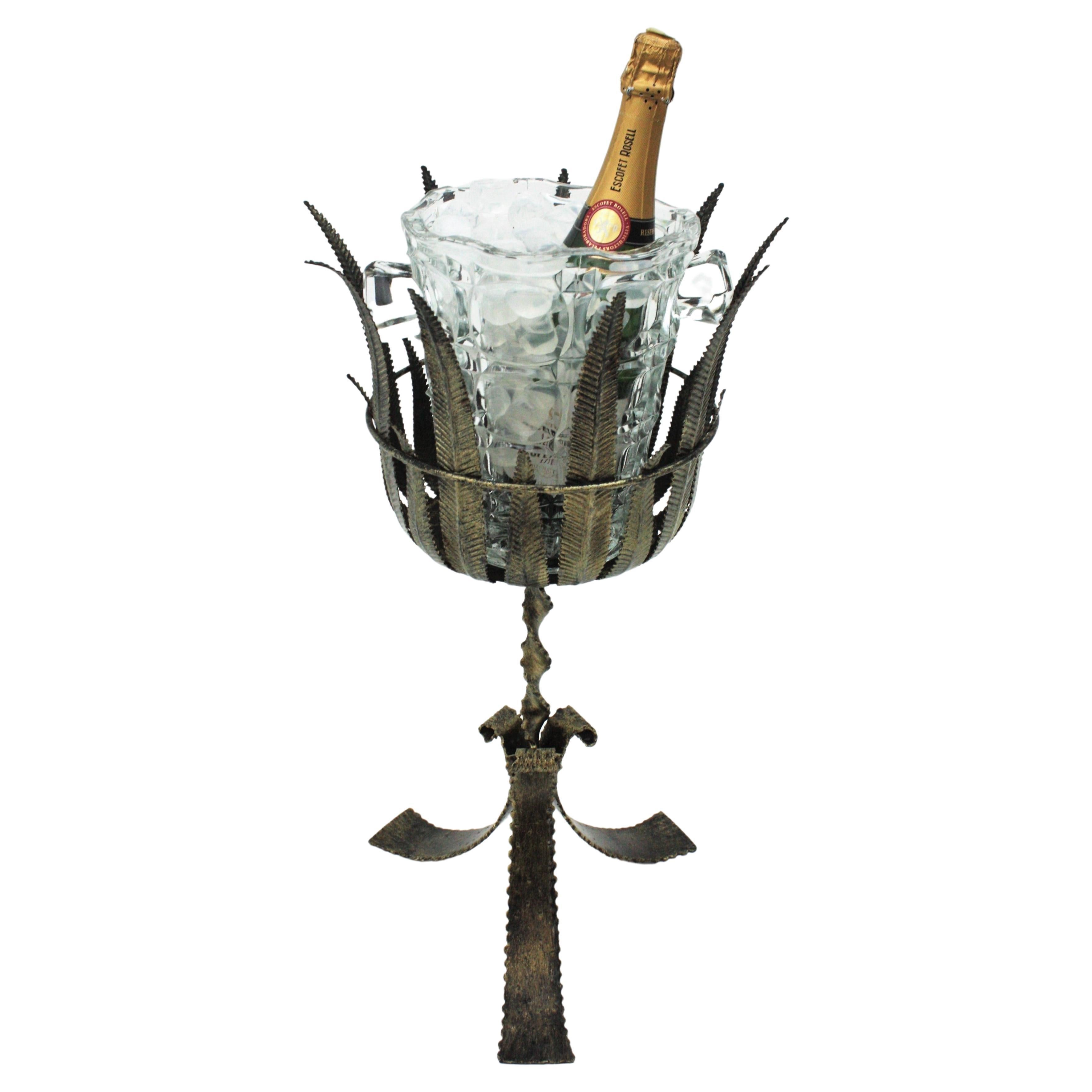 Soporte trípode único de hierro dorado con follaje y cubitera de cristal prensado, España, años 40
Esta cubitera de hierro para servir está hecha a mano. El soporte de hierro forjado a mano tiene una tapa de hojas ricamente adornada que se apoya en