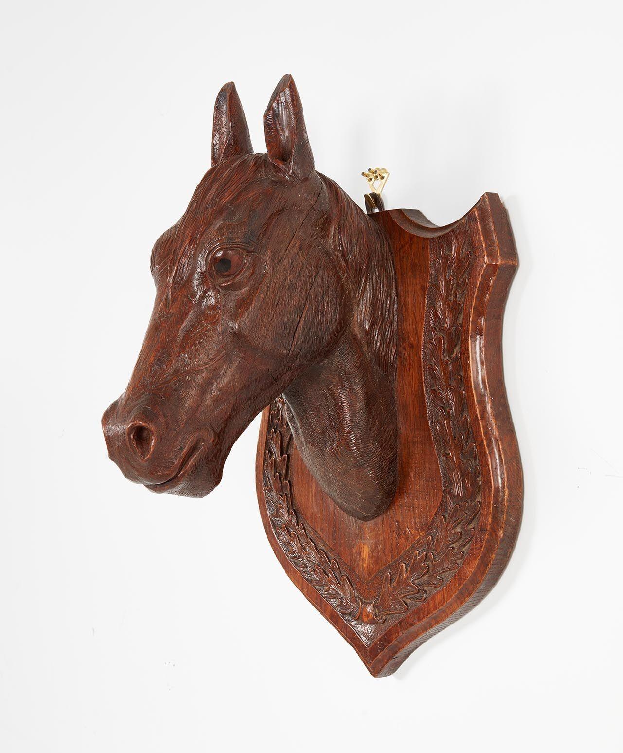 An equestrian stable mascot of a champion horse, finely sculpted in English oak, capturing his alert, expressive face, with great attention to detail. Glass eyes. Mounted on a shield with carved laurel wreath border. Very good patina.