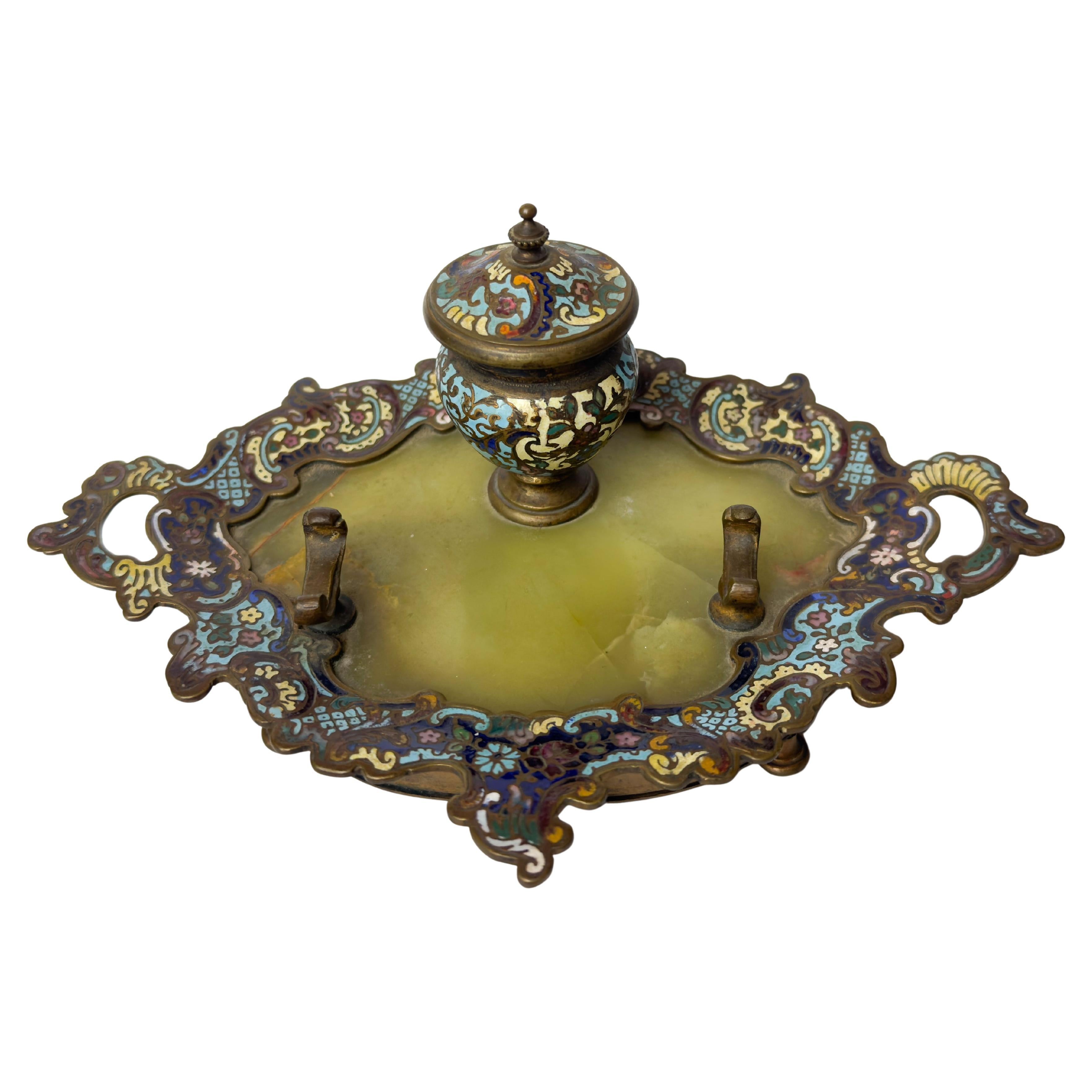 A 19th century French inkwell in Champlevé enamel and bronze, mounted on an integrated tray with pen holders, in the Napoleon III style. 
This elegant desk accessory showcases the craftsmanship and aesthetic richness 19th Century.

The inkwell is