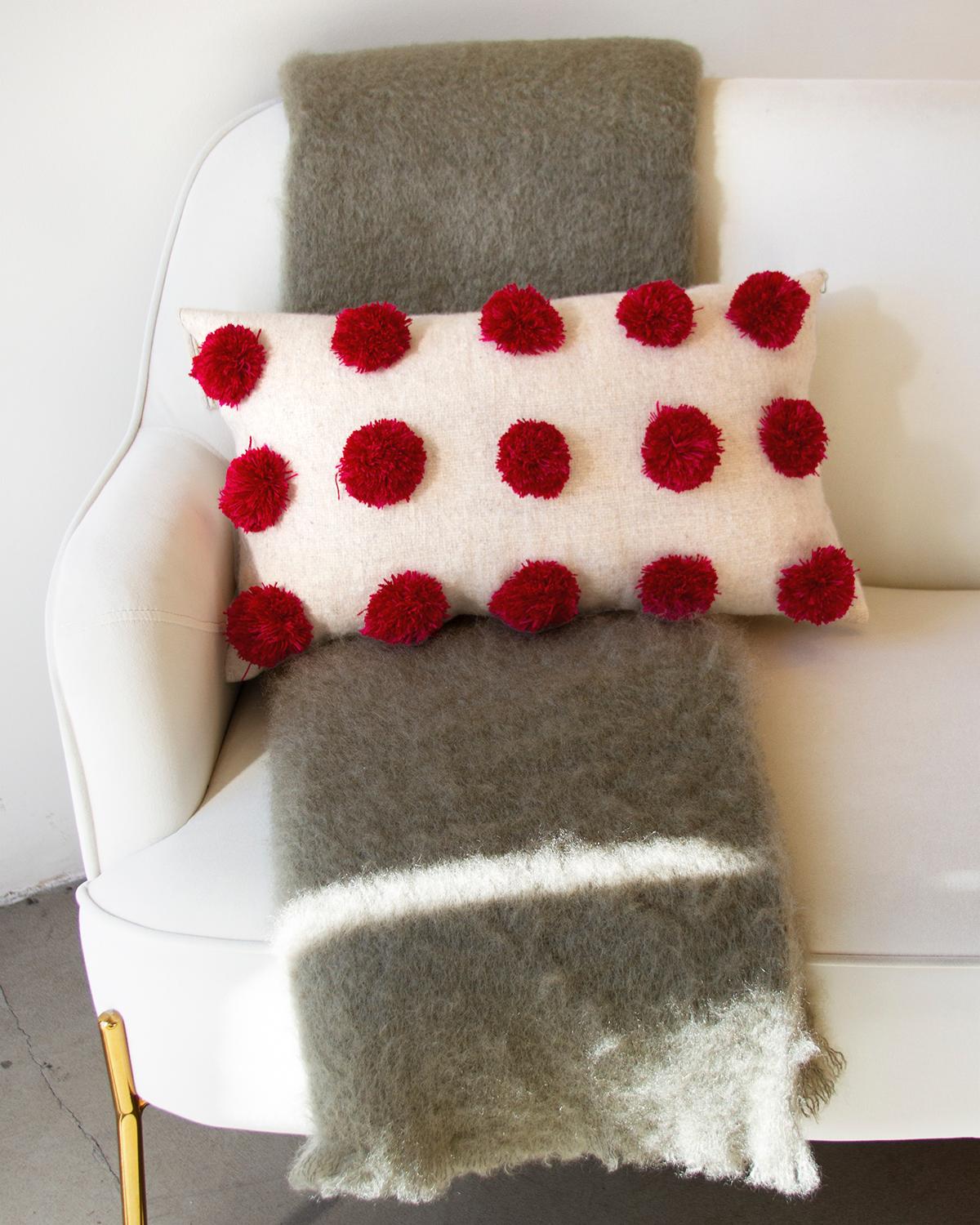 Add some subtle and elegant holiday vides to your home decor
This lumbar pillow from Chamula blends rustic charm with subtle holiday cheer. Crafted from wool, it features a white base with red pompom accents, ideal for seasonal decorating and