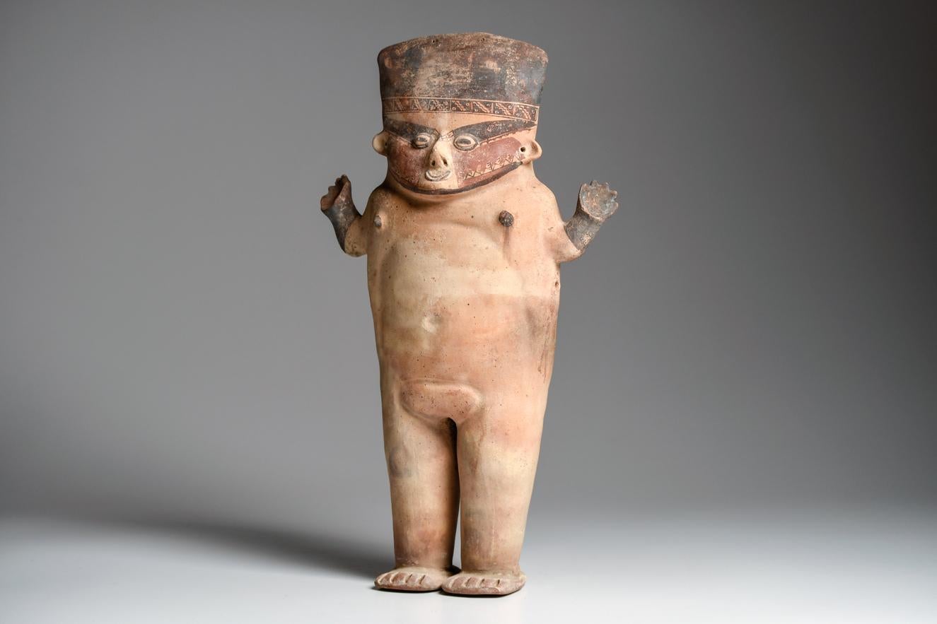 Cream slip pottery, large standing female figure with arms raised. Nicely painted red and chocolate-brown face, with a finely detail geometric headband. Scattered mineral deposits on the surface. Feet restored, repaired from approximately fifteen