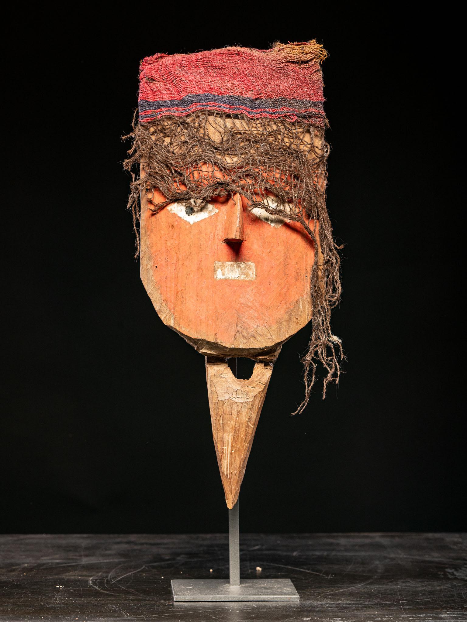 A hand-carved funerary mask meant to attach to a larger mummy bundle. The plank-form mask is painted with a broad red face accented with white, diamond-shaped eyes, a rectangular mouth, and a prominent nose. The top of the head is perforated for