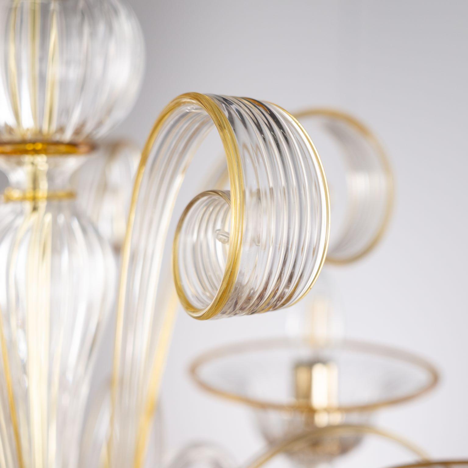 Capriccio Kronleuchter, 5 Lichter, aus klarem Kunstglas, mit geschwungenen Ornamenten und bernsteinfarbenen Details von Multiforme.
Es ist von der klassischen venezianischen Tradition inspiriert und zeichnet sich durch eine zentrale Säule aus, in