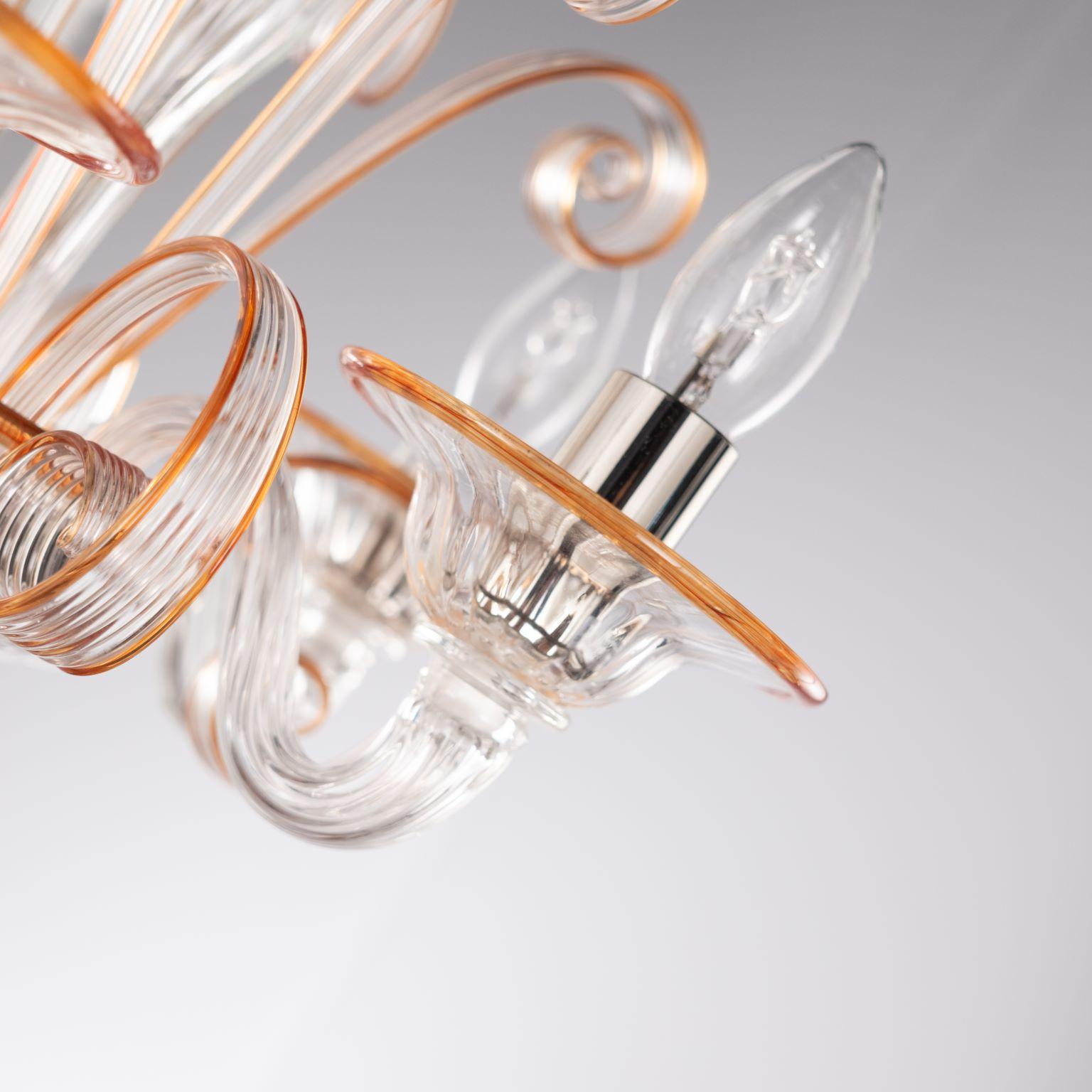 Capriccio chandelier, 5 lights, in clear artistic glass, with curly ornamental elements and orange details by Multiforme.
Inspired by the Classic Venetian tradition it is characterised by a central column where many blown glass “pastoral” elements