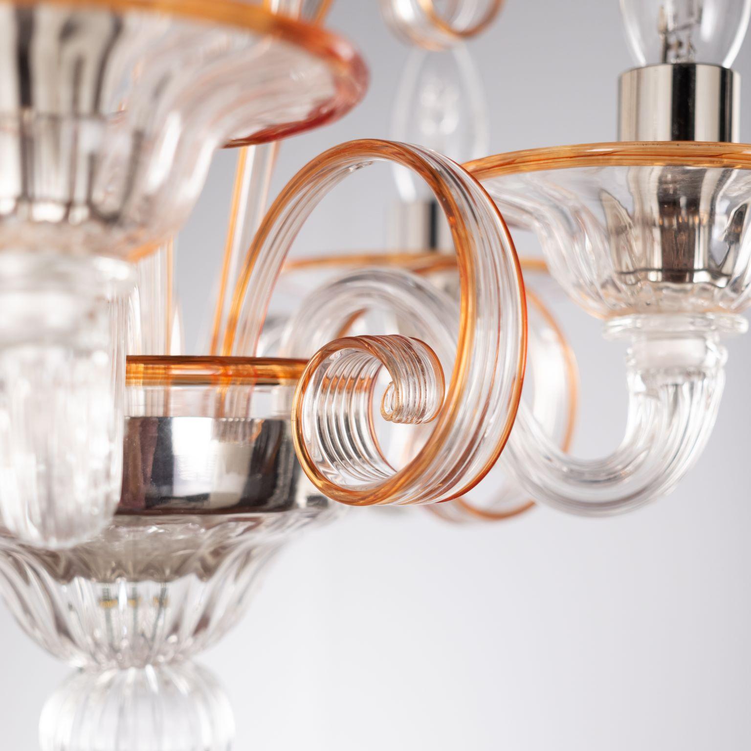 Lampadario Capriccio, 5 luci, in vetro artistico trasparente, con elementi ornamentali ricci e dettagli arancioni di Multiforme.
Ispirata alla tradizione classica veneziana, è caratterizzata da una colonna centrale in cui sono installati molti