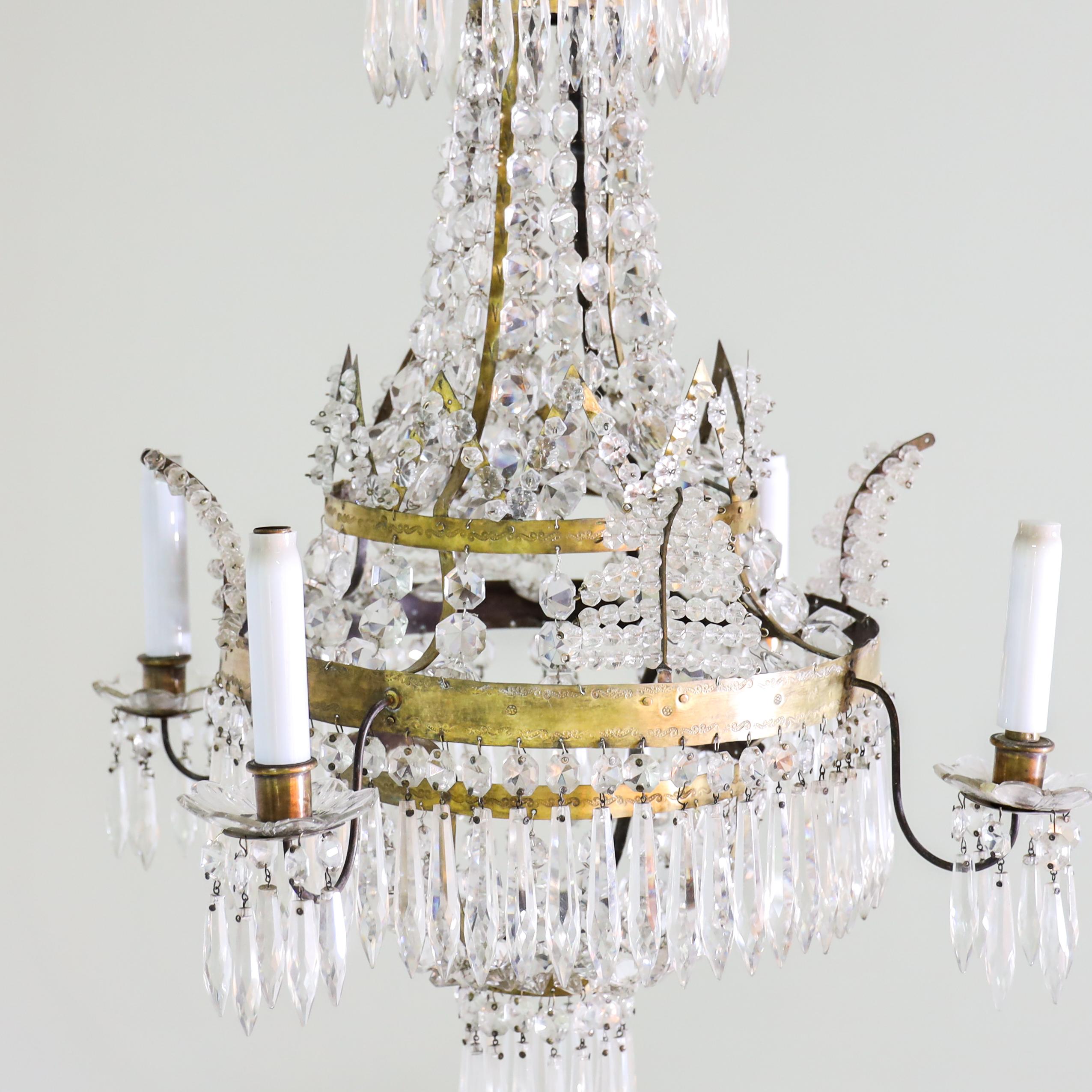 Four-light ceiling chandelier with crystal glass hangings and multi-level structure of brass hoops. The flower-shaped drip bowls are also made of glass and hung with glass prisms.