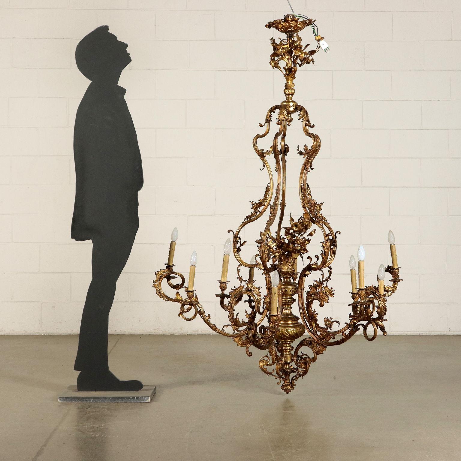Big gilded bronze chandelier. It has five wavy bipartite arms and ten light spots. Richly decorated with wide spirals, leaves and flowers. Turned central body.
