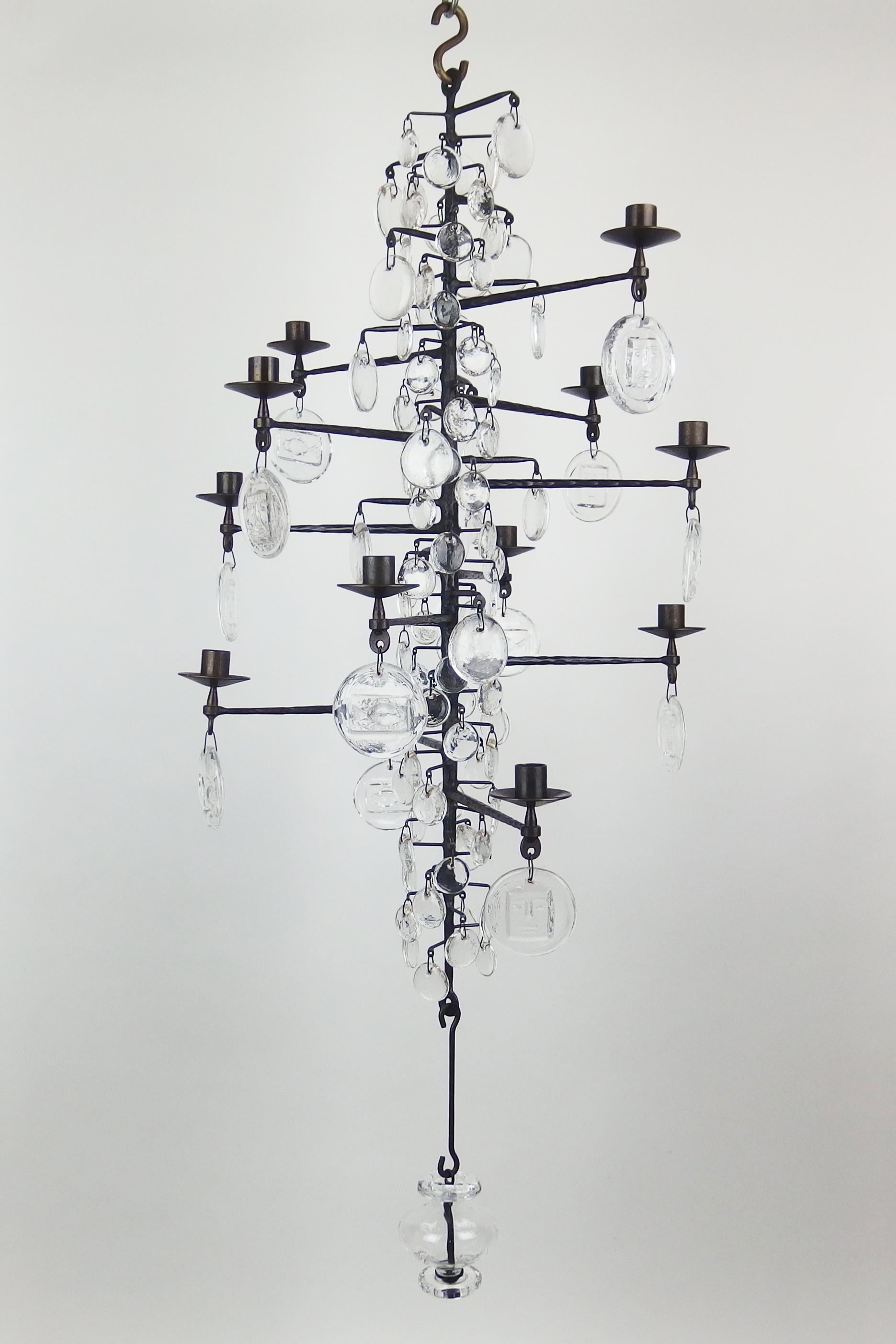 A dark grey enameled cast iron candelabra chandelier with 12 arms and 3 sizes glass pendants, the larger pendants with stylized face or fish patterns. Made by Boda Smide for Erik Hoglund.