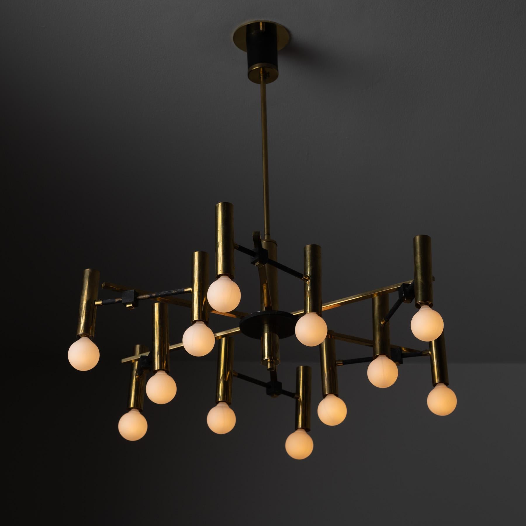 Chandelier by Arteluce. Designed and Manufactured in Italy, circa the 1950s. Naturally aged brass throughout with black enameled accents on joints and canopy. Rewired for US standards. Takes twelve E14 60 watts max bulbs. Bulbs provided as a one