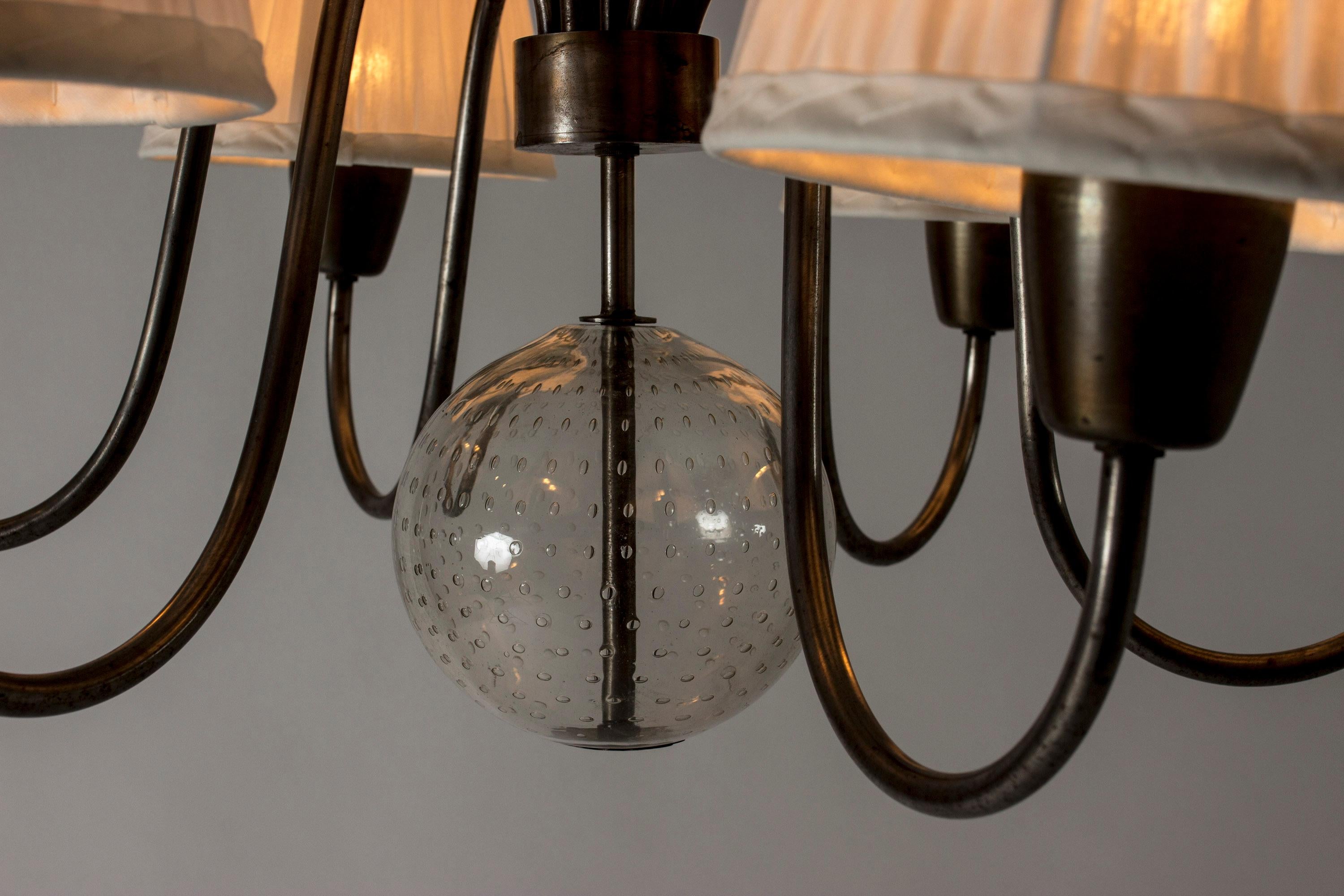 Beautiful chandelier by Hans Bergström, with six curved arms coming out from the center. Glass sphere with air bubbles makes a very decorative, floating element in the middle. Pleated white shades, chain suspension.

Hans Bergström was the owner