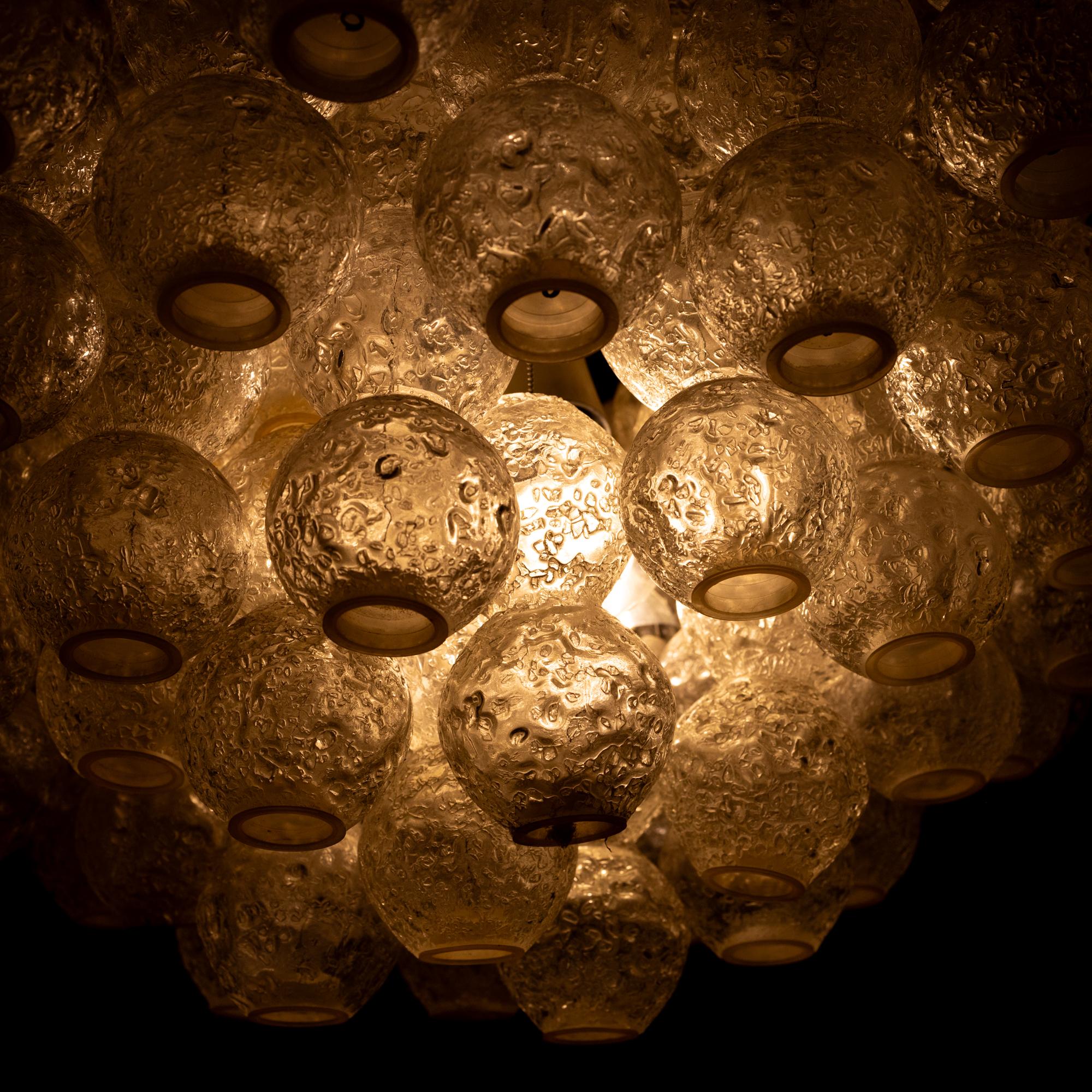 Large ceiling lamp with glass bodies of clear ice glass arranged in the form of rays, which are suspended from thin link chains. The spherical glass bodies made of Murano glass join together to form a cloud-shaped whole.