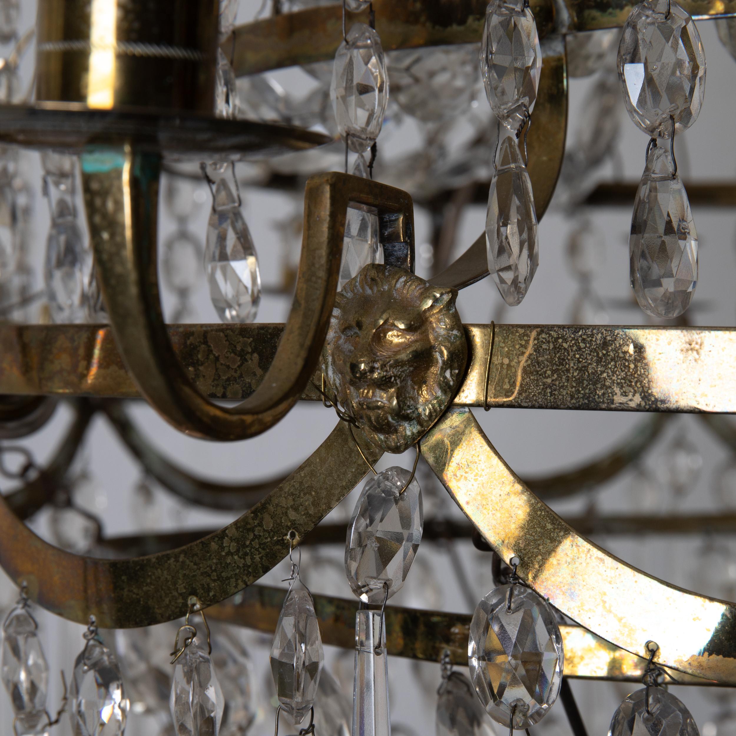 Lustre Chrystal suédois Gustavien néoclassique en laiton Suède. Un lustre fabriqué au début du 19e siècle. Prismes en cristal sur un corps en laiton. Décoré de têtes de lions. 12 bras pour bougies et une 