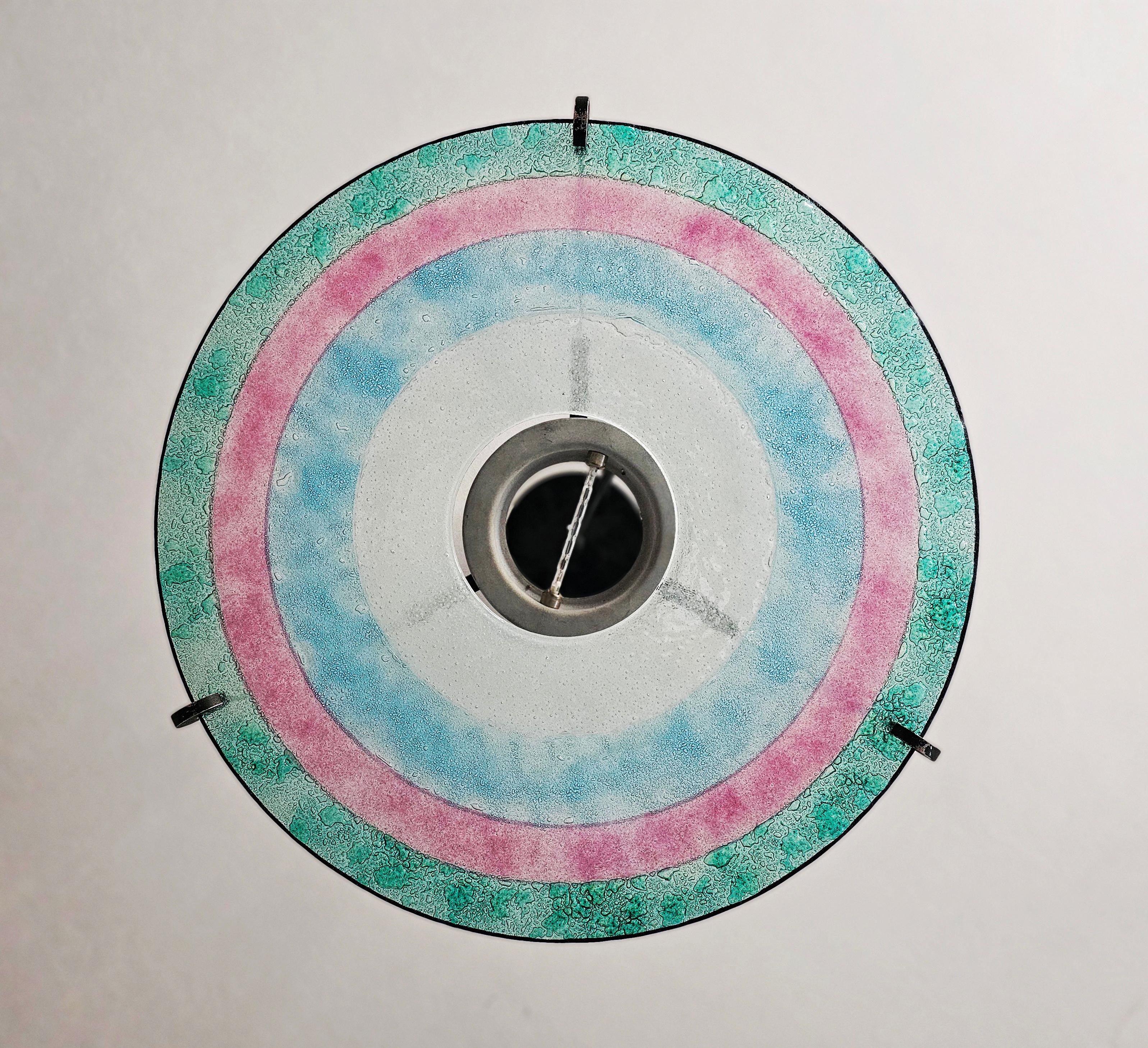In this listing you will find a very special chandelier designed in style of Memphis Group inspired by the Rings of Saturn. It features a large, flat circular plate done in multiple colors of glass with texture. The height of the chandelier is