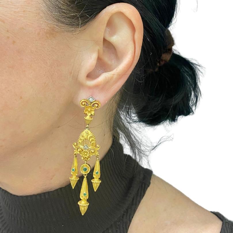 A pair of spectacular chandelier earrings from the Victorian era, made of 14k gold, featuring emerald.
These chandelier earrings showcase intricate metalwork, blending delicate floral and scroll motifs with geometric elements. The upper part