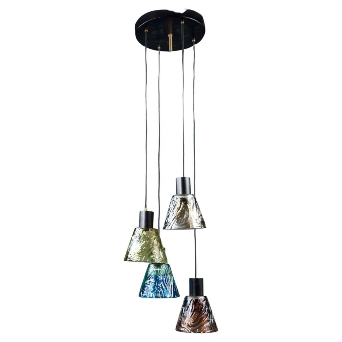 Four handblown, colorful glass shades, conic in shape with textured outer walls, suspended from round ceiling plate.


