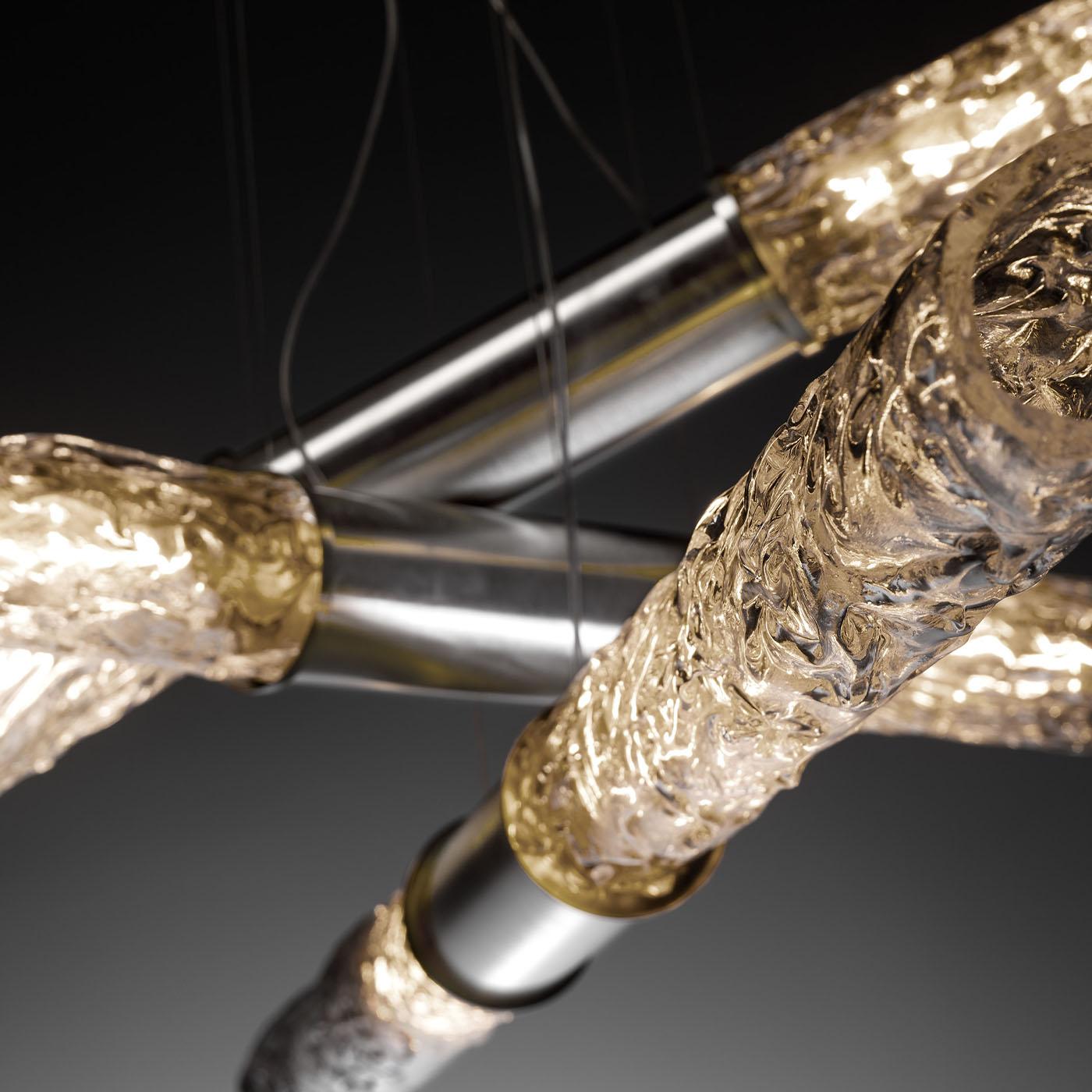 A stunning blend of artistry and illumination, this modern revisitation of a classic chandelier is designed to enchant. The sleek metal frame supports three overlapping arms with a central metal core and sublime mouth-blown glass ends with a