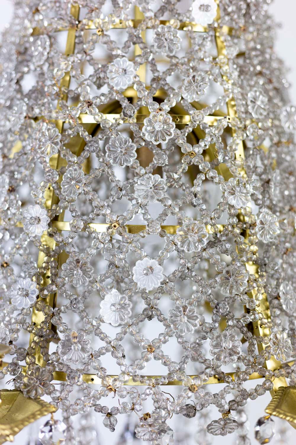 Lustre en forme de dentelle composé de perles de cristal ornées de fleurs en cristal. Lampes à six bras décorées de feuilles d'acanthe placées sur un rang attaché à l'axe central. Cache-belière (crochet de cuir) en forme de couronne fermée à fleur
