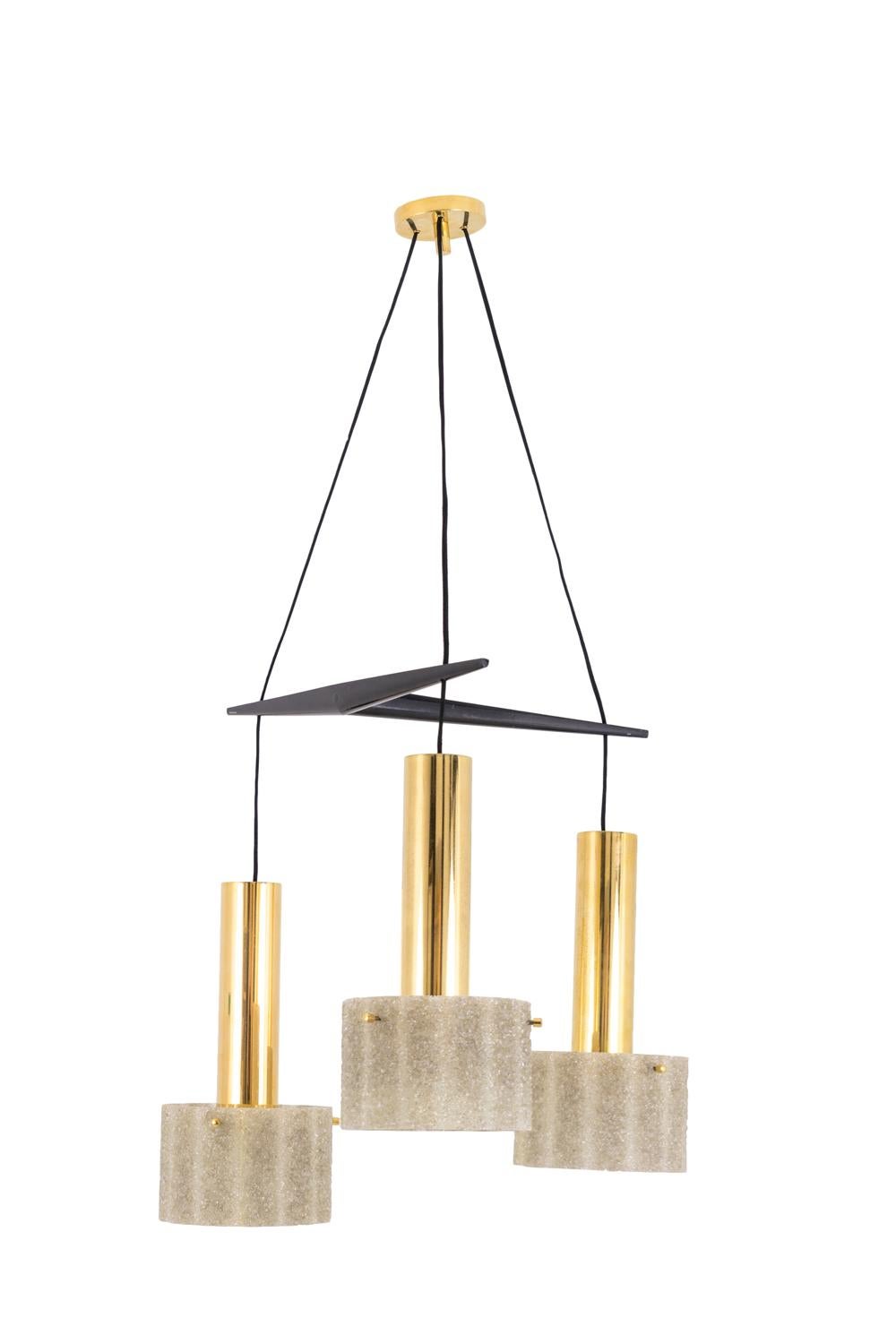 Lampadario in resina di granito e ottone dorato composto da tre mobili luminosi appesi tramite fili a una struttura geometrica in legno laccato nero. Mobili con fusti cilindrici in ottone dorato e paralumi cilindrici in resina di granito.

Opera
