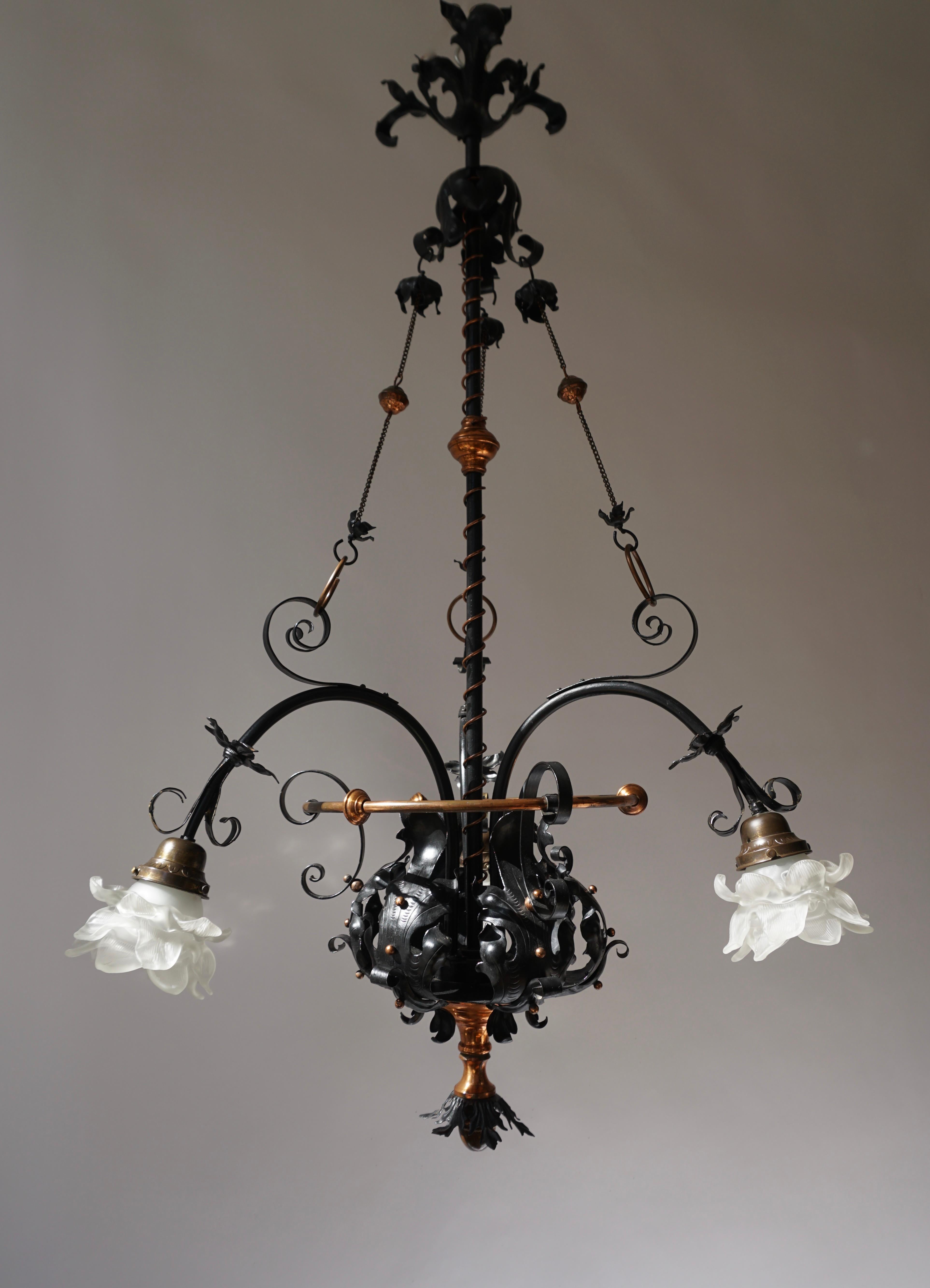 Extraordinary decoratif chandelier, made of wrought-iron and brass, carrying leave-motifs and with three arms, each with a glass cap. 
The iron being stained black and the brass guilt.
The light requires three single E27 screw fit