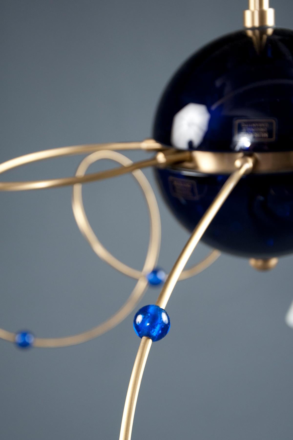 Eight spiralling brass arms, with spherical blue glass beads and white glass diffusers, issue from a central sphere of blue glass; suspended from a single stem with a brass star element and canopy.