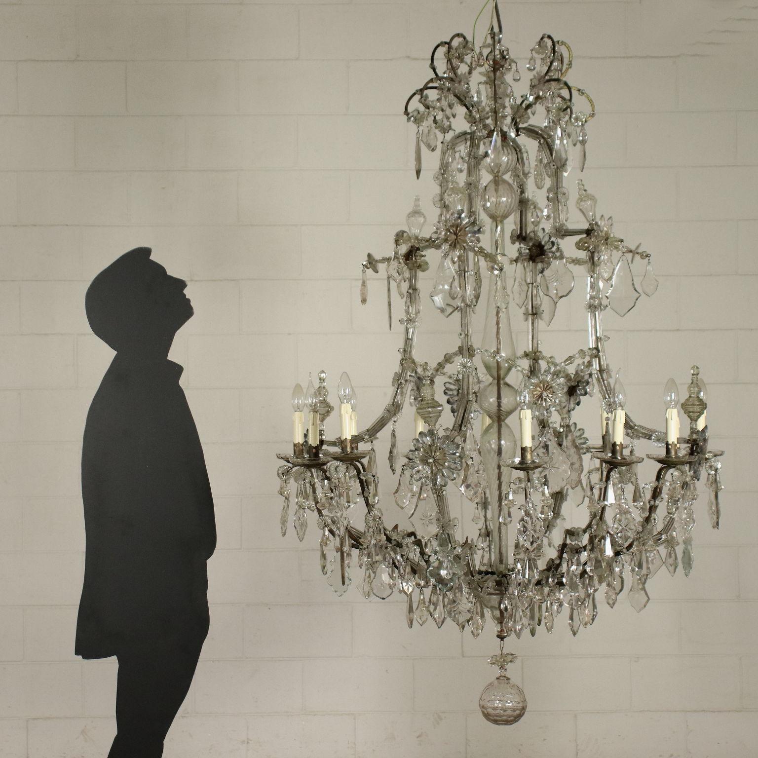 Marie Theresa chandelier with 12 lights, dating back to the end of the 18th century. Iron branches, the supporting ones are covered in glass, the bobeches are in cast bronze. The chandelier is adorned with bevelled glass pendants and adorned with