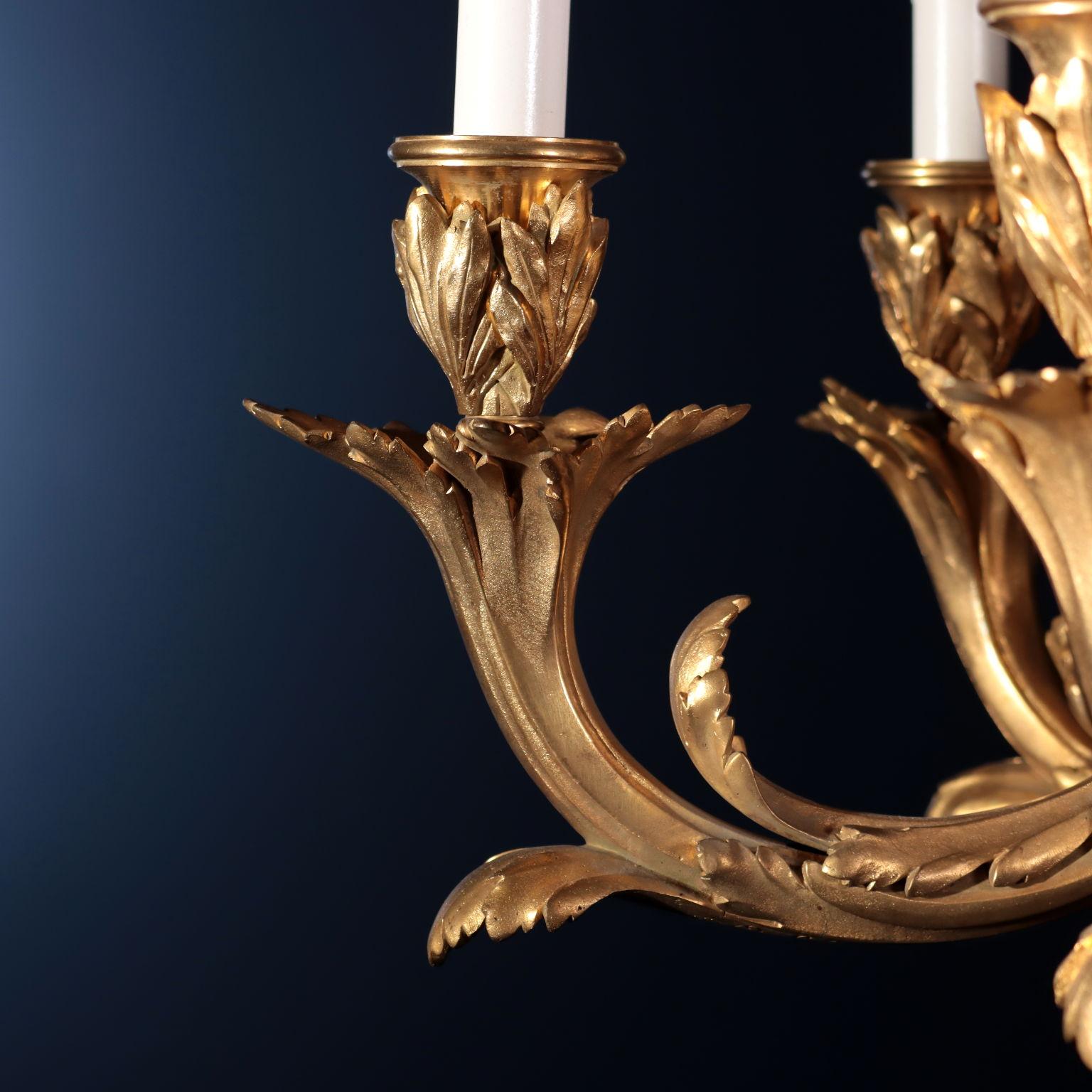 Chandelier with six lights in gilded bronze, it presents a central baluster that ends with a cone, and it is decorated with leaf-like motifs and laurel branches; it is decorated with a bunch of grapes in the lower part. Six branches embellished with