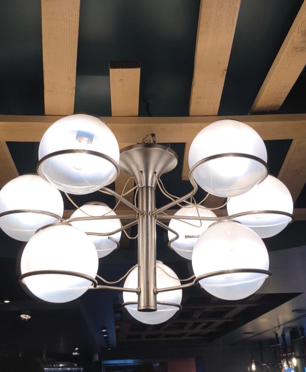 Araña/colgante con nueve difusores de metal y cristal opalino, probablemente diseñada por Gino Sarfatti y fabricada por Arteluce en Italia en la década de 1960.
.
Un orbe resplandeciente rodeado por un anillo metálico, suspendido en el aire, casi