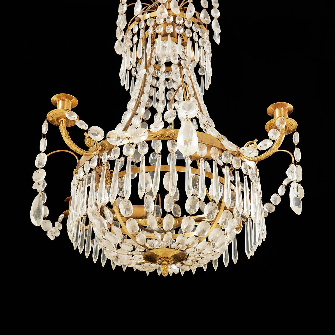 Un lampadario della metà del XX secolo progettato per contenere quattro candele. Realizzato con una struttura in ottone e ornato da una serie di prismi in vetro tagliato.
Sul lampadario, situato dietro i cristalli, c'è spazio per 5 lampadine.