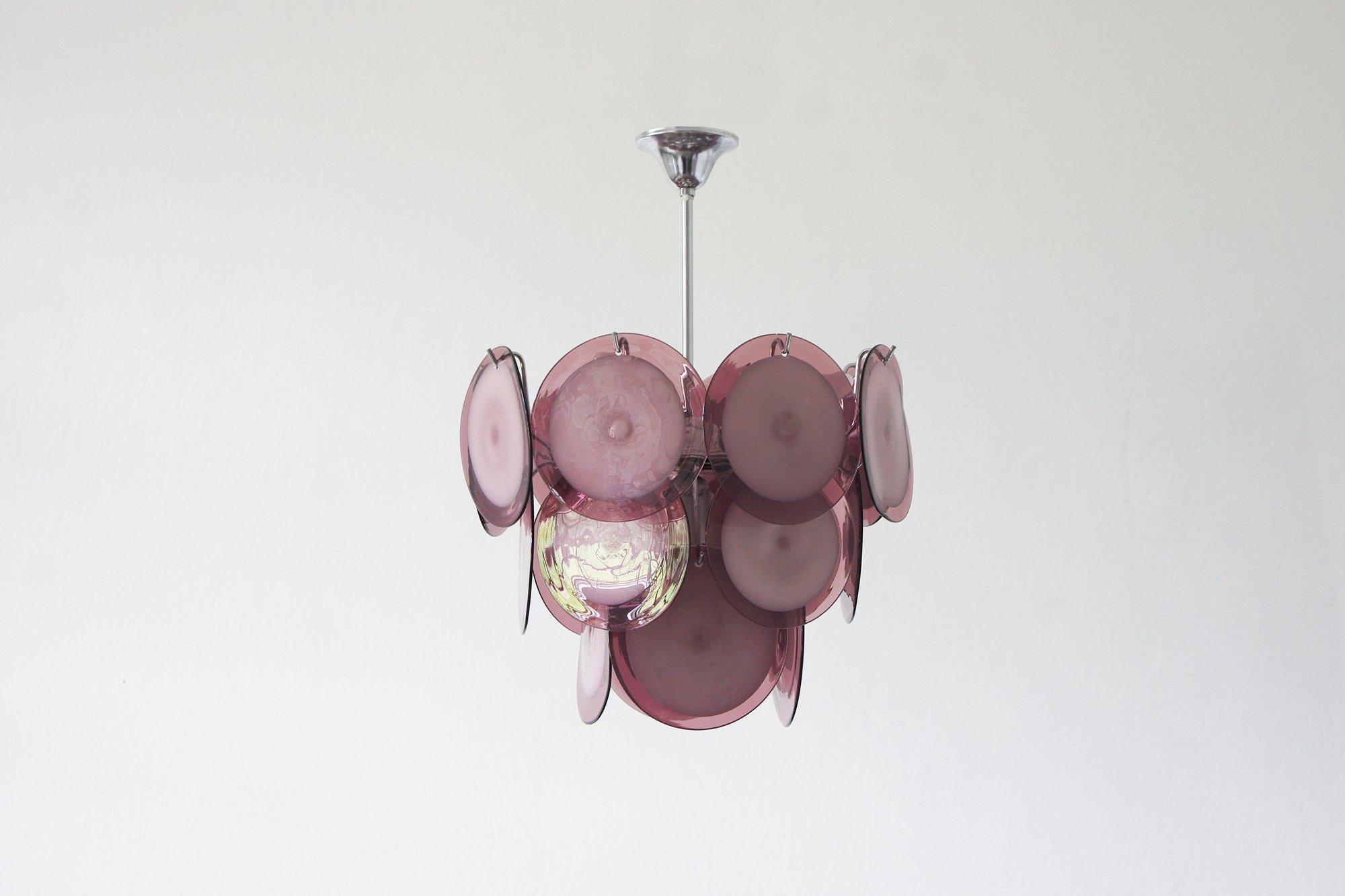 Lustre en verre de Murano conçu par Mazzega dans les années 1960.
19 pièces de disques en verre de Murano soufflés à la main dans des tons de violet et de blanc.
Le tout suspendu à un cadre chromé.

Un lustre d'une beauté et d'une élégance rares