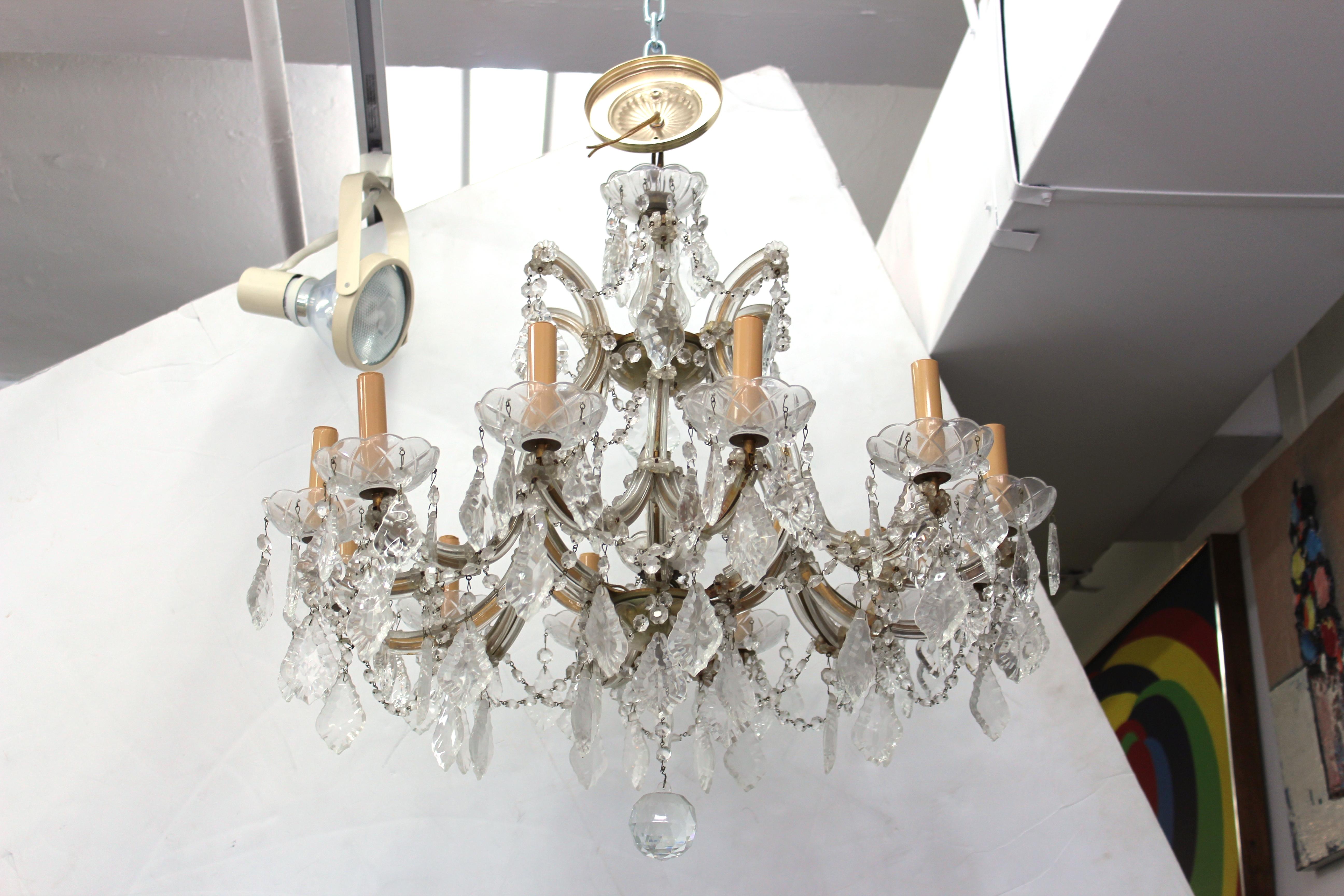 Chandelier with 12 arms in clear cut-glass and crystal. Each arm features a faux candle socket and is draped with cut crystal beads. Large cut crystal drop hang throughout. Some wear includes missing droplets on lower tear appropriate to age and