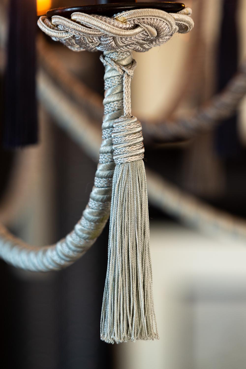 Wrought iron structure is wrapped with jute and silk cording. From an elaborate cap, fifteen arms descend at three staggered heights and depths, alternating in colors. Cording under the bobèche is shaped in traditional passementerie knotted detail.