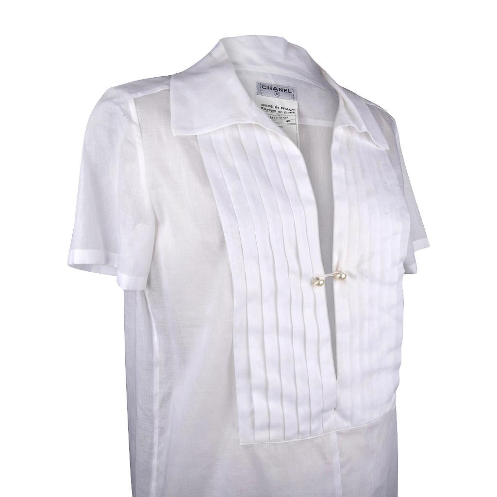 Guaranteed authentic Chanel 04C gossamer light white cotton top. 
White semi sheer cotton top with a plunging V.
Front has tuxedo pleating and 2 small pearl buttons that catch in the center.
Buttons are embossed Chanel and are very subtle.
Hem has a