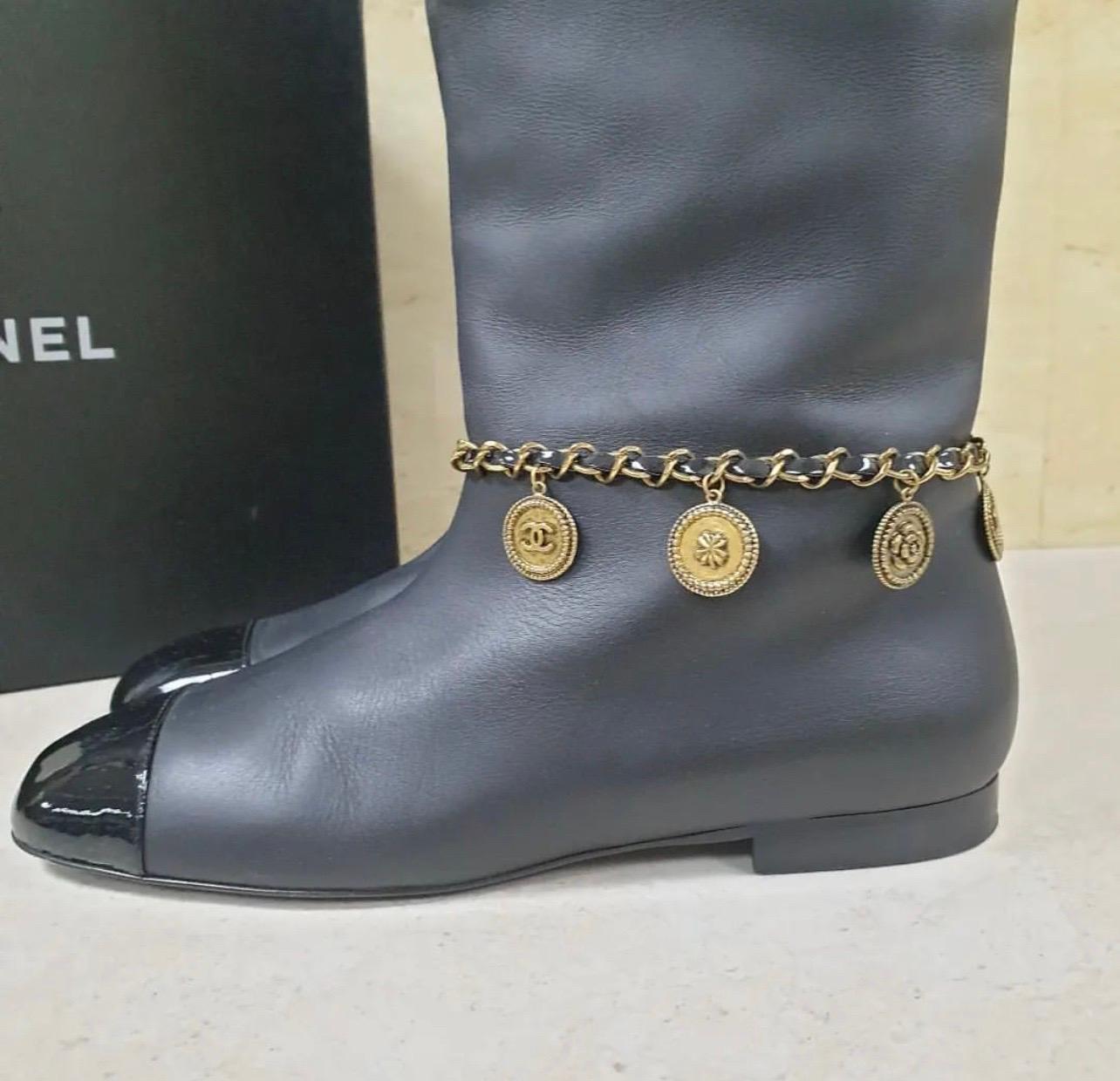 CHANEL black leather tall boots. These flat boots have a signature patent leather cap toe. The ankle has the signature chain link around it with gold toned, iconic Chanel charms (the ‘CC’ logo, camellia flower, four leaf clover etc).