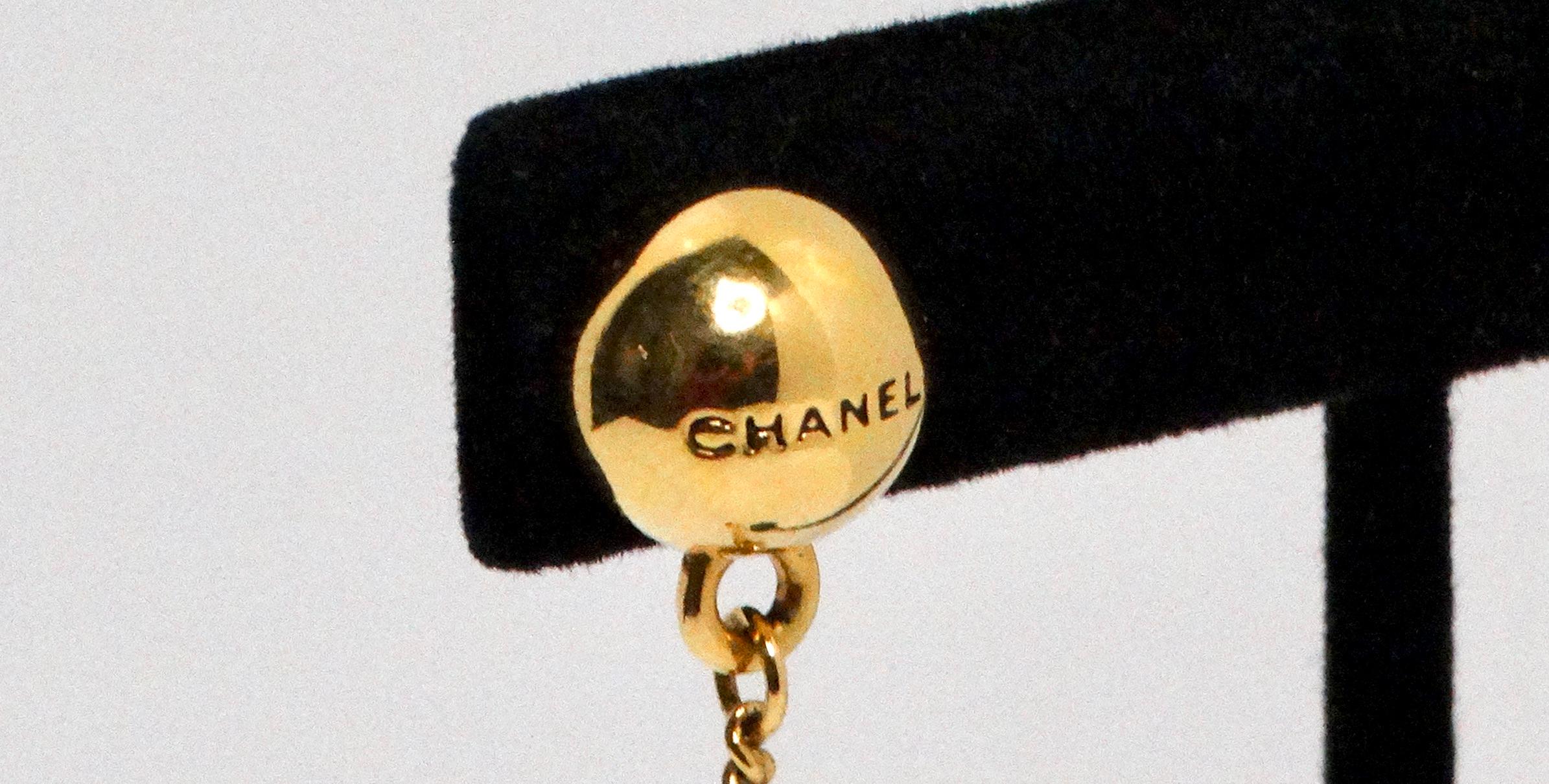 The Chanel 18k Gold Plated Ball Charm Drop Earrings are a striking example of the brand's signature elegance and timeless style. These earrings feature a gold-plated finish, with the top ball adorned with the iconic 