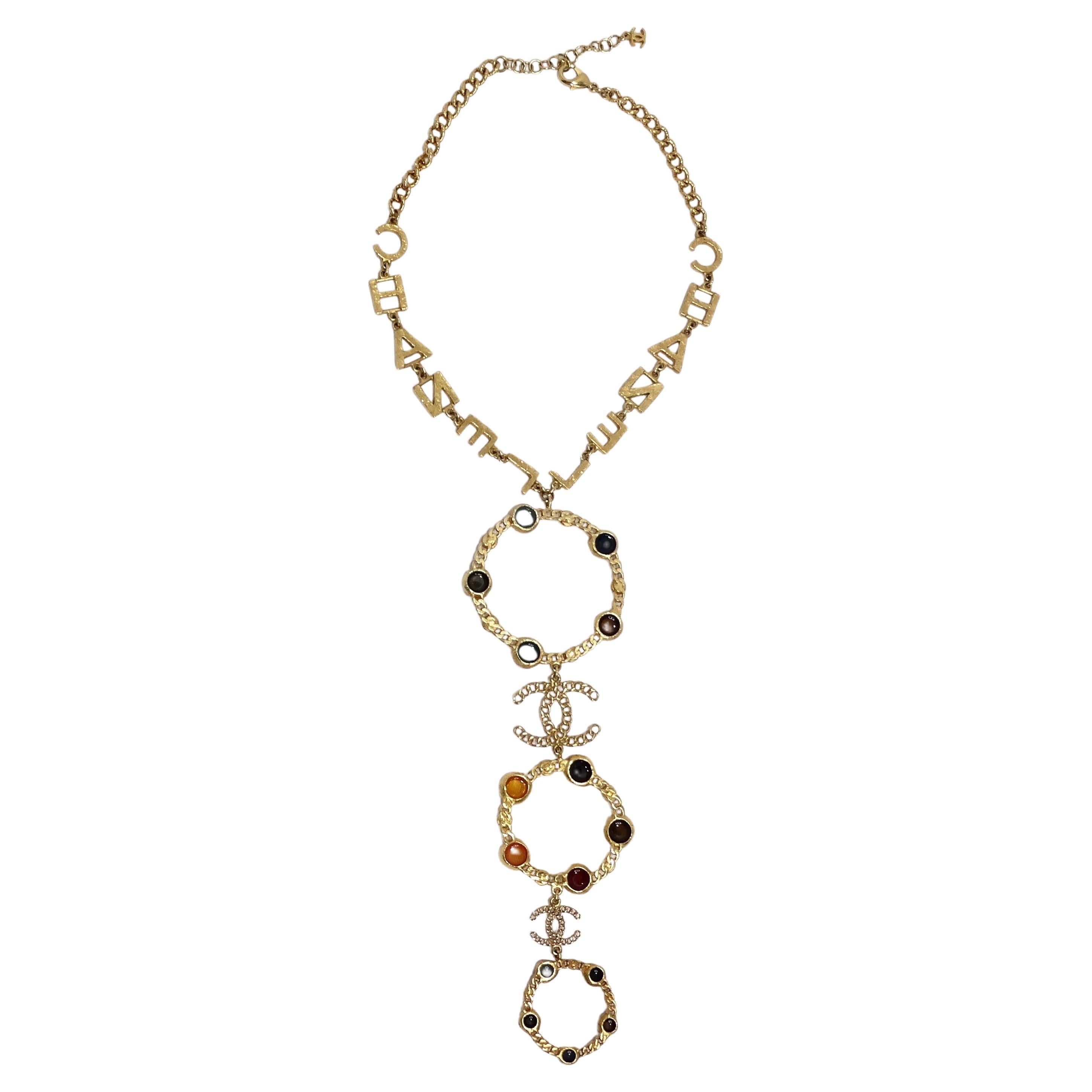 Introducing the Chanel 18K Gold Plated Logo Multi Gemstone Lariat Necklace, a true masterpiece of luxury and elegance. This extraordinary statement piece is a reflection of timeless beauty and sophistication. Chanel is synonymous with style and