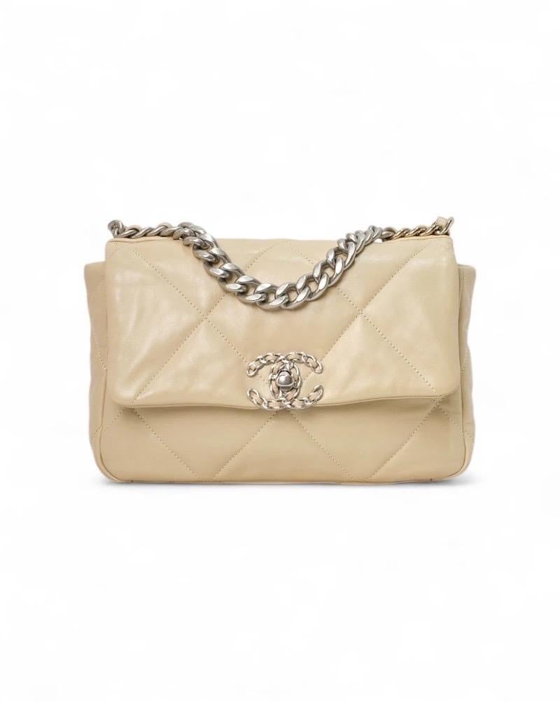 Borsa firmata Chanel, modello 19 Flap nella misura small, realizzata in pelle trapuntata beige con hardware bicolor, oro/argento. La patta frontale è arricchita dal classico logo del brand “CC” in metallo e chiusura a girello. Internamente rivestita
