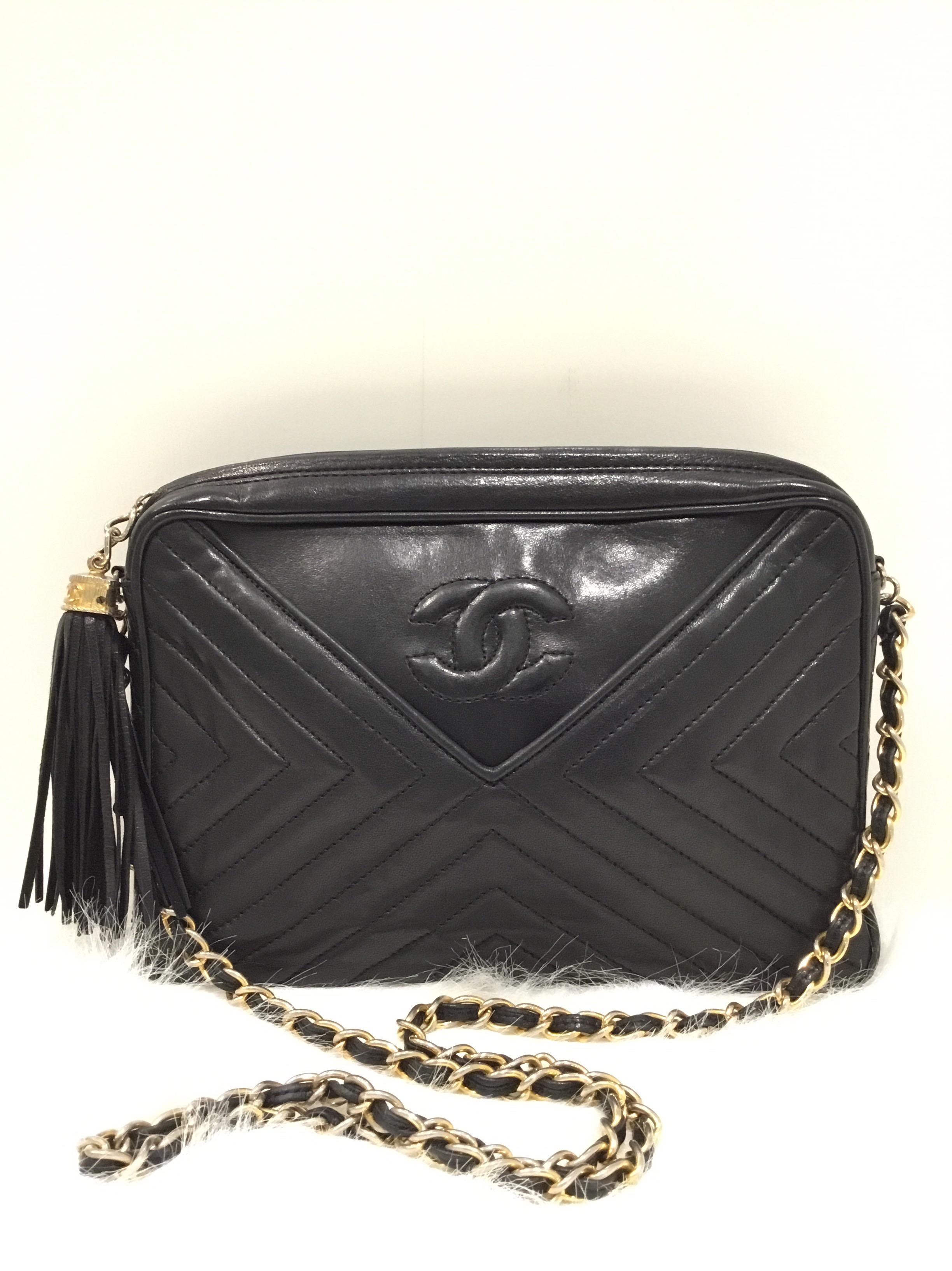 Vintage Chanel camera bag featured in black lambskin leather with a Chevron design. Bag has a front pocket, goldtone chain intertwined with leather strap that has a drop measuring 17 inches, top zipper fastening with a leather tassel zipper pull, a