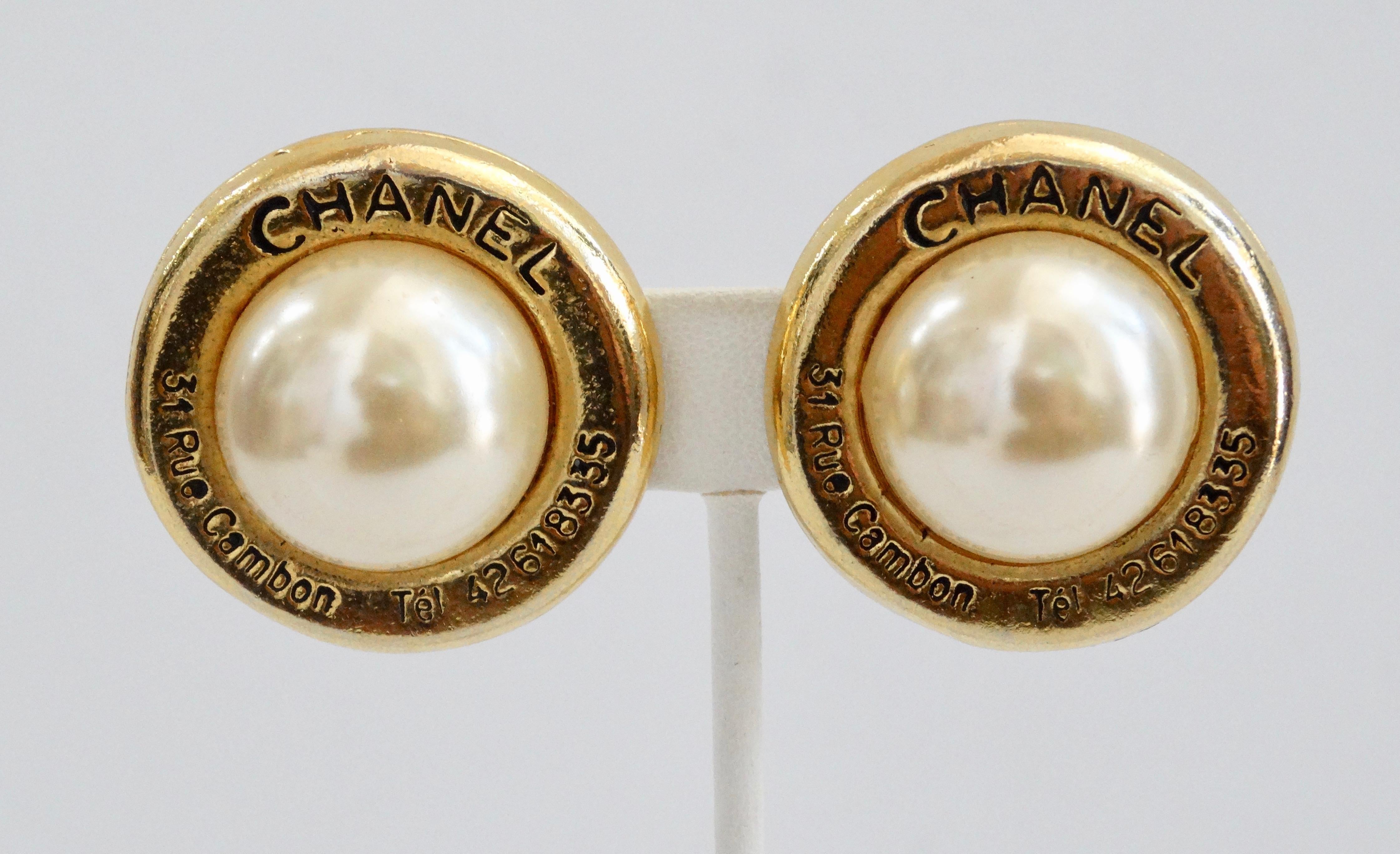 Complete your jewelry collection with these Chanel earrings! Circa 1980s, these classic earrings are gold plated, set with a large faux pearl and are embossed with the Chanel address and telephone number. Includes clip-on closures and are stamped