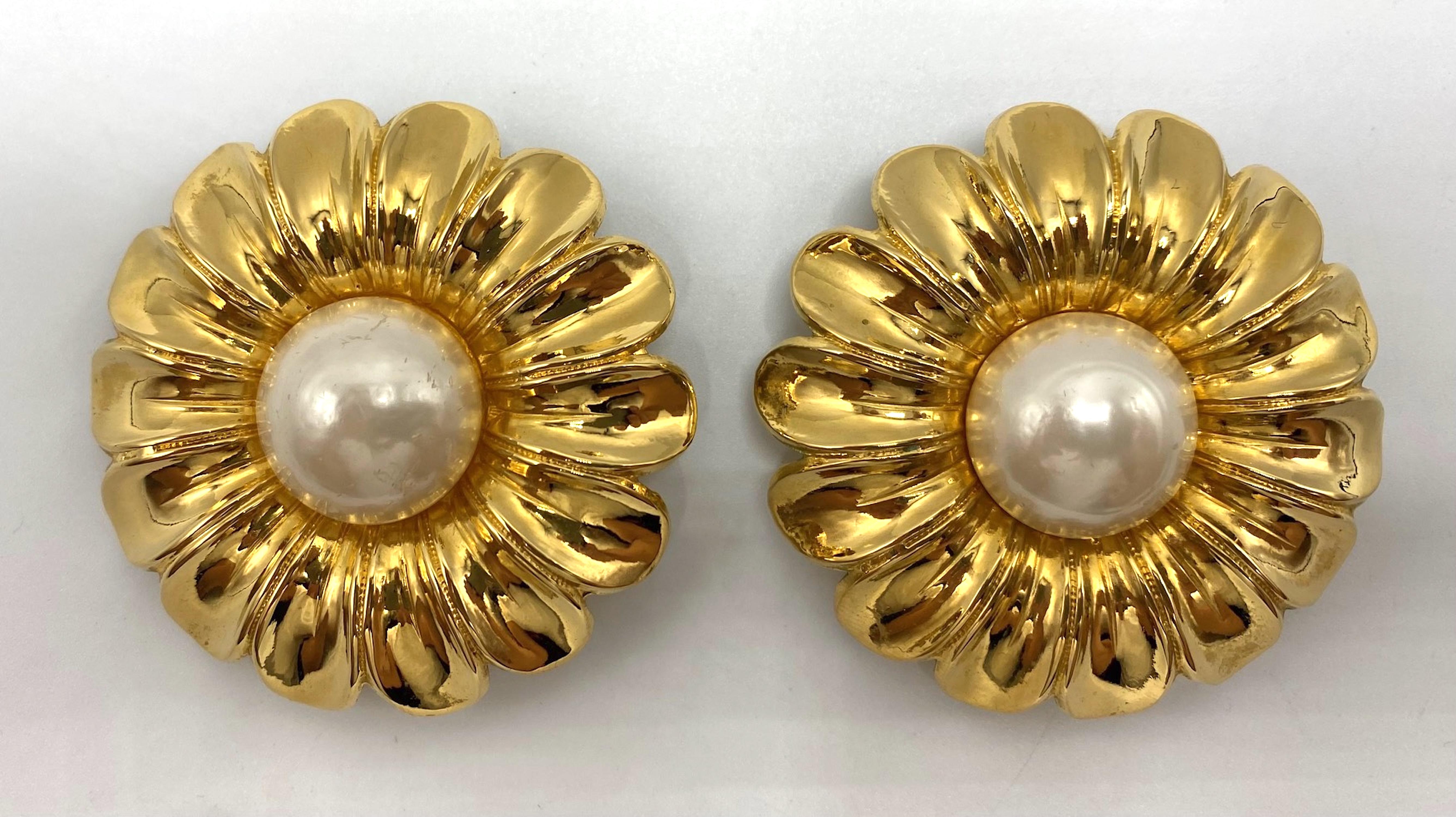 Presented is a pair of mid 1980s large gold margarita flower earrings by Chanel. The clip earrings are done in bright 18K gold plate with a faux Baroque pearl cabochon center. Each earring measures 2.38 inches in diameter and .5 of an inch high.
