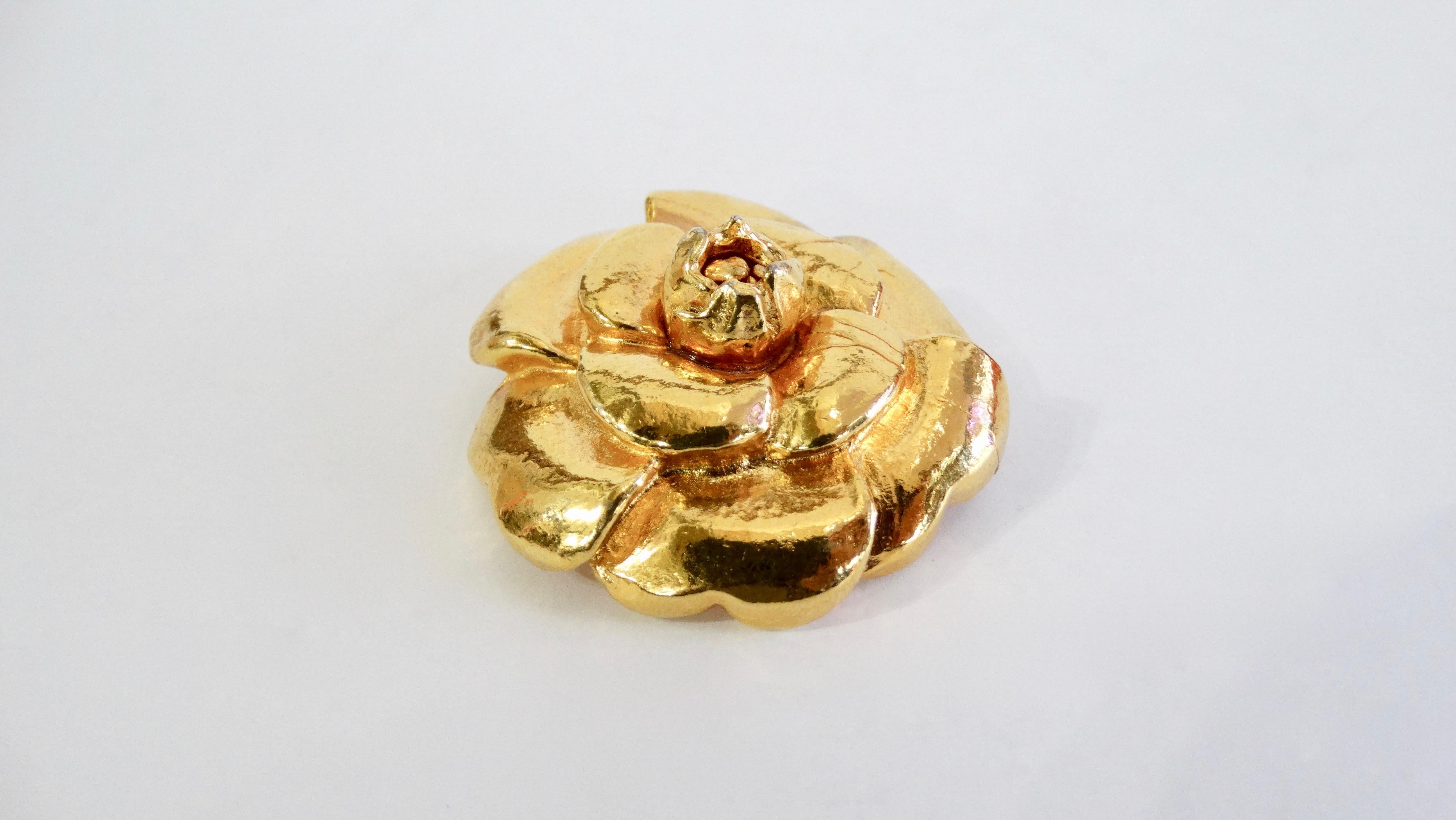 Every Chanel girl needs something with the Camellia flower! Circa late 1980s, this metal brooch is plated in gold and has been crafted into the signature Chanel Camellia flower. Stamped and signed. The perfect Chanel piece to wear on your favorite
