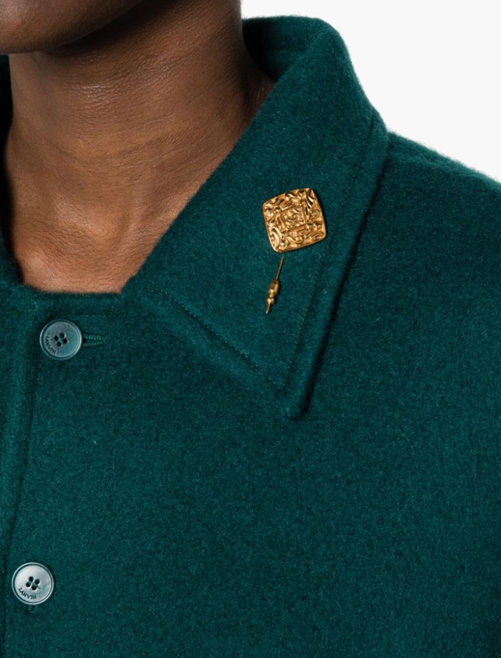 Goldfarbene diamantförmige Brosche von Chanel mit folgenden Eigenschaften: diamantförmiges, ineinandergreifendes, geprägtes CC-Logo auf der Vorderseite, geprägte Details, eingraviertes Logo auf der Rückseite, Verschluss mit Stiften. 
CIRCA 1980er