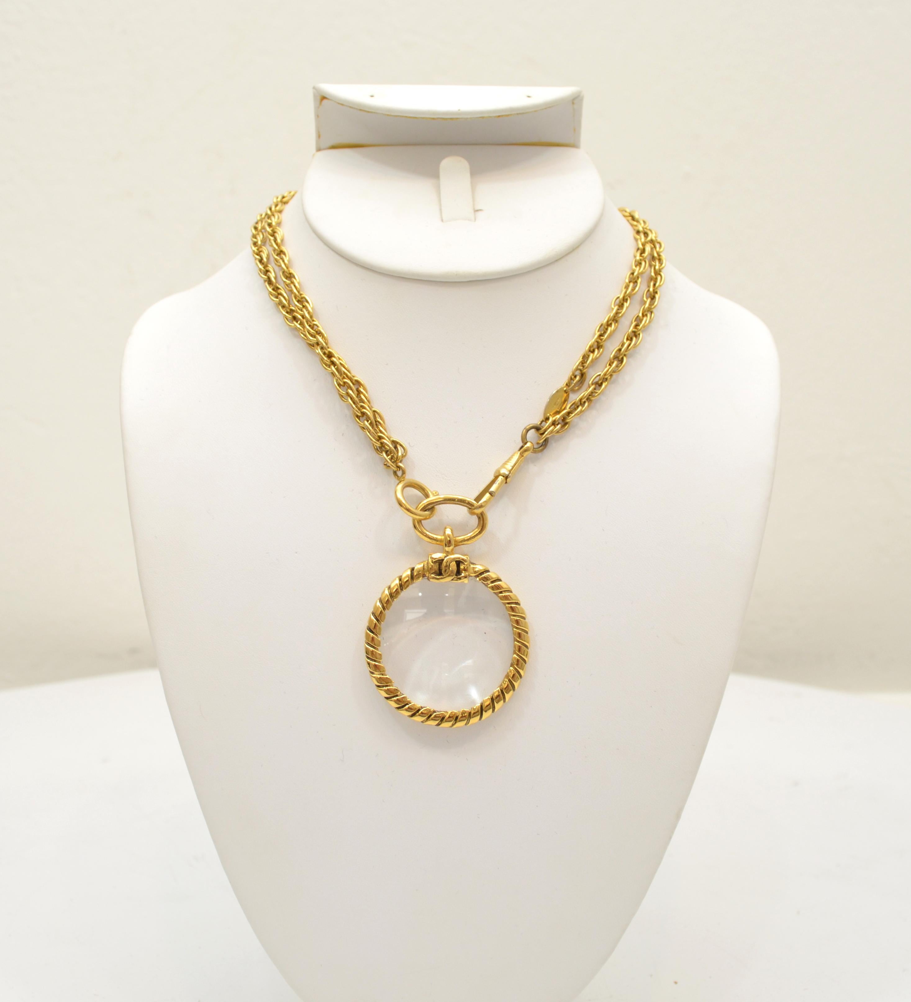 This stunning vintage Chanel necklace, part of the first collection produced by Karl Lagerfeld as Creative Director of Chanel in 1983, showcases an elegant magnifying glass pendant with a 24k gold plated wrapped metal border with a CC logo at the