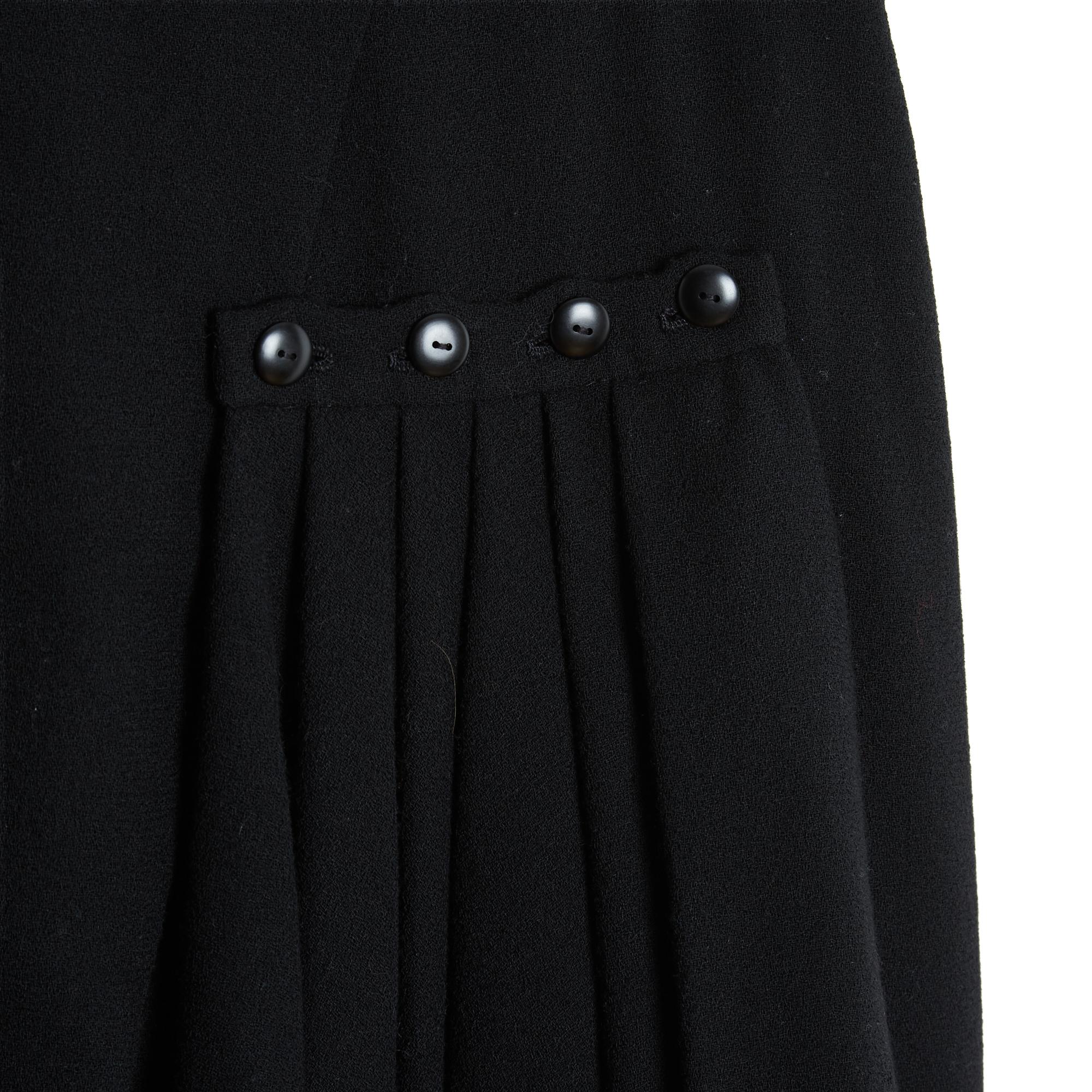 Gonna Chanel Haute Couture del 1985 in crepe di lana nera, a vita alta con chiusura a zip e gancio, forma a matita impreziosita da un drappeggio a pieghe trattenuto da quattro bottoni sul davanti, fodera in seta nera. Non ci sono etichette di