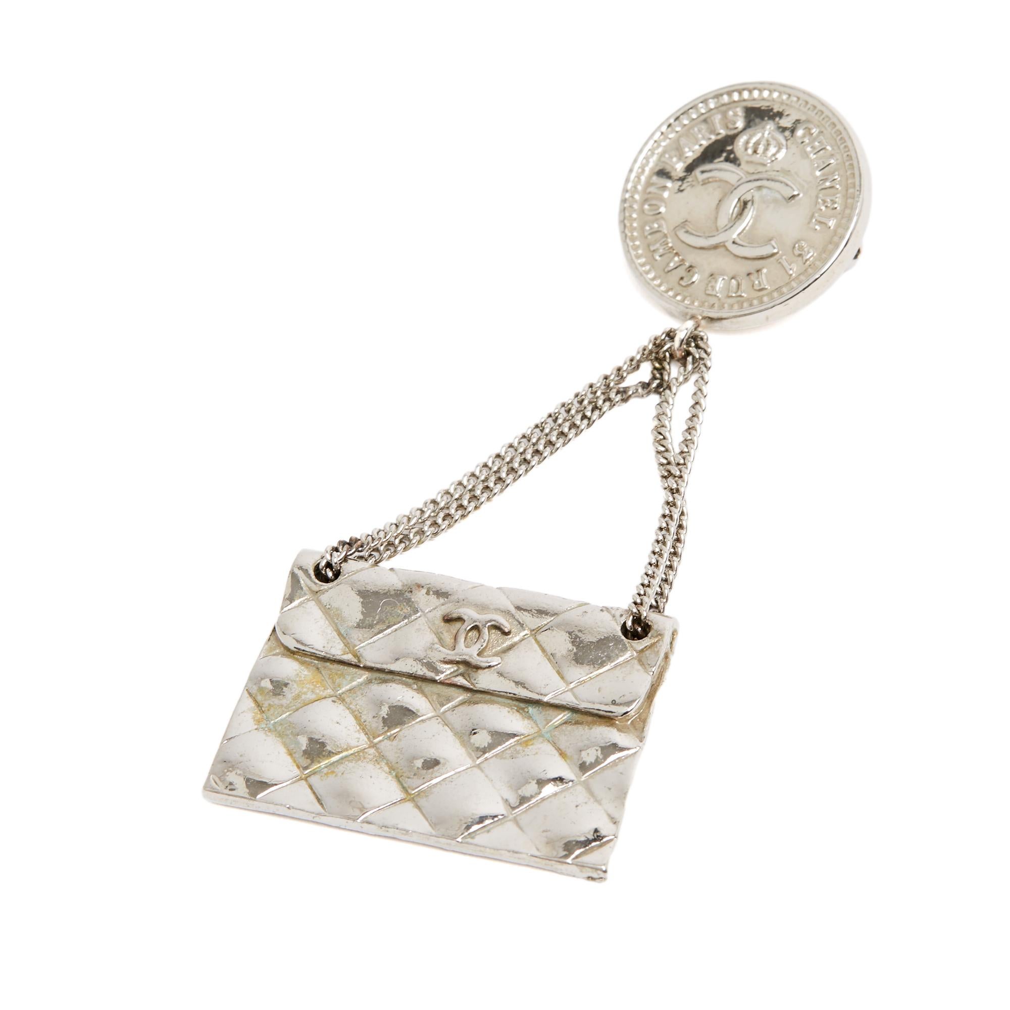Spilla Chanel collezione PE 1990 in metallo color argento con un motivo a medaglione CC e un ciondolo, attaccato da 2 catene, con il motivo della borsa trapuntata Chanel Timeless o Classique su una tracolla ... Altezza 8 cm x larghezza 4,65 cm. La